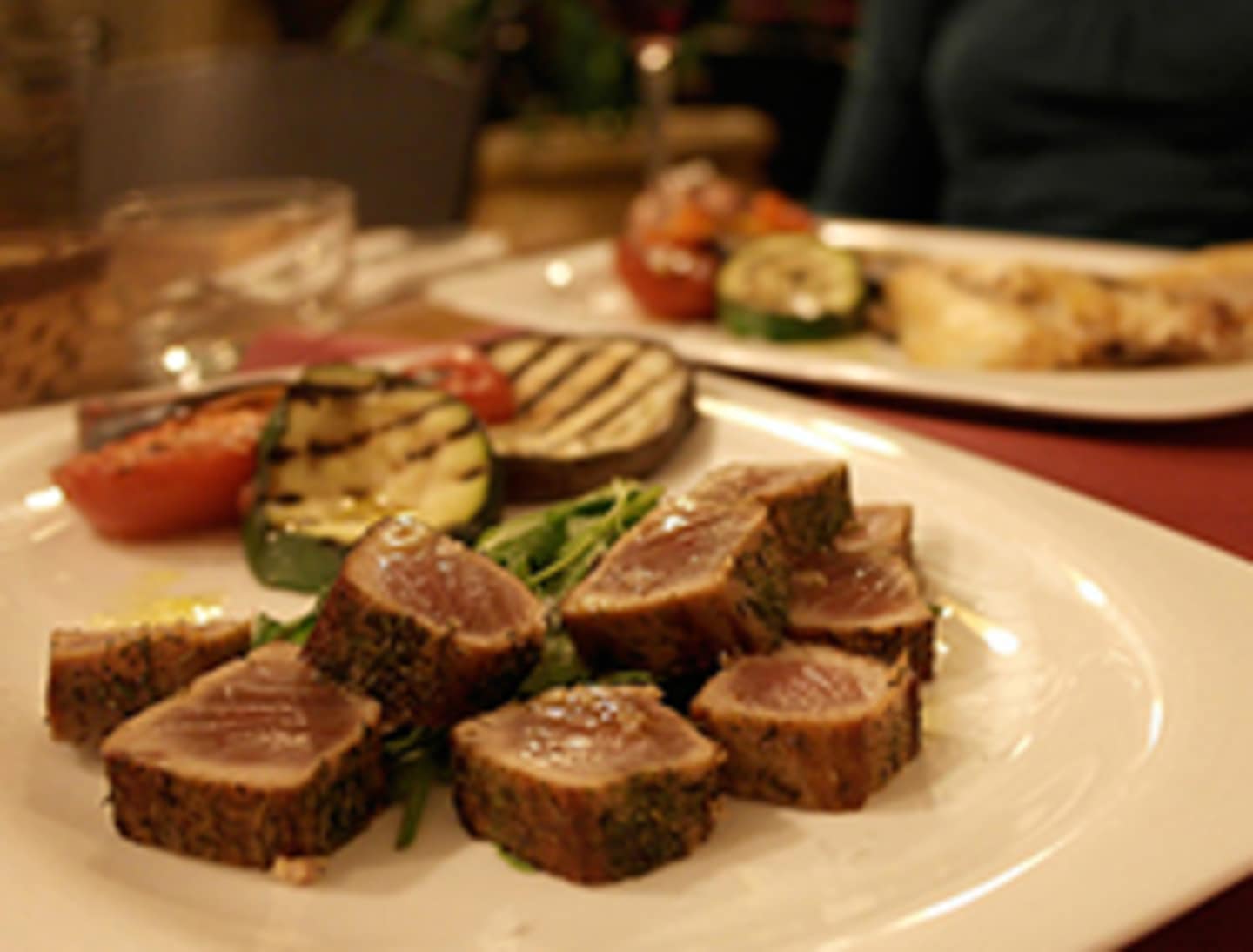 A plate filled with various appetizers, including sliced meat, grilled vegetables, and what appears to be a cheese board, set against a dimly lit background.