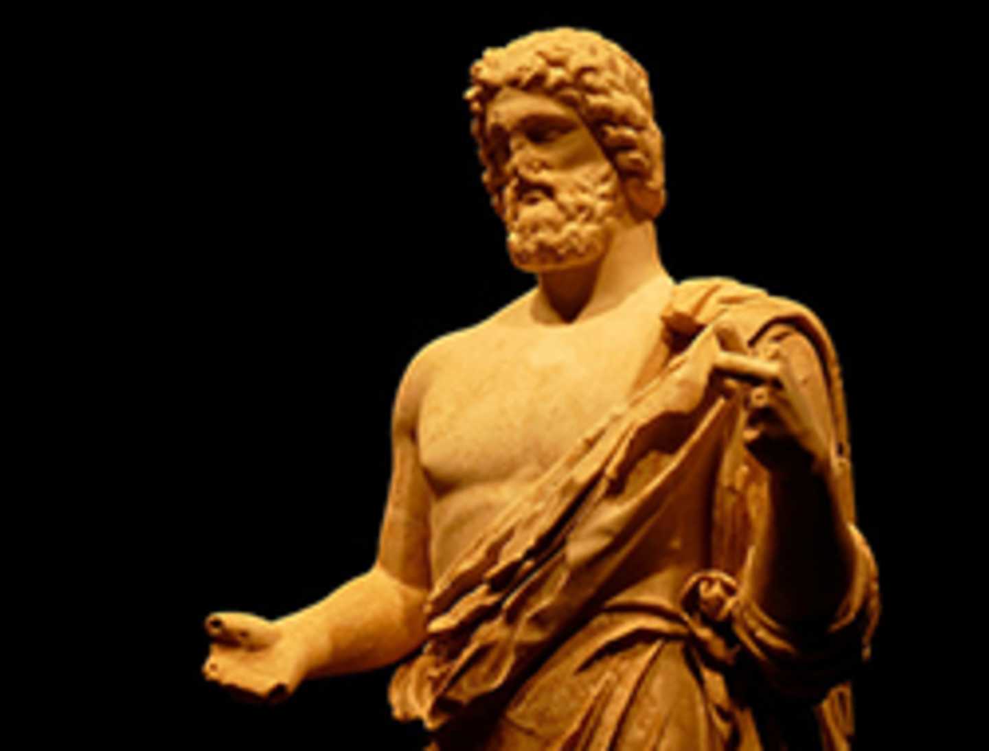 A marble statue of a bearded male figure in a flowing robe stands against a dark background.