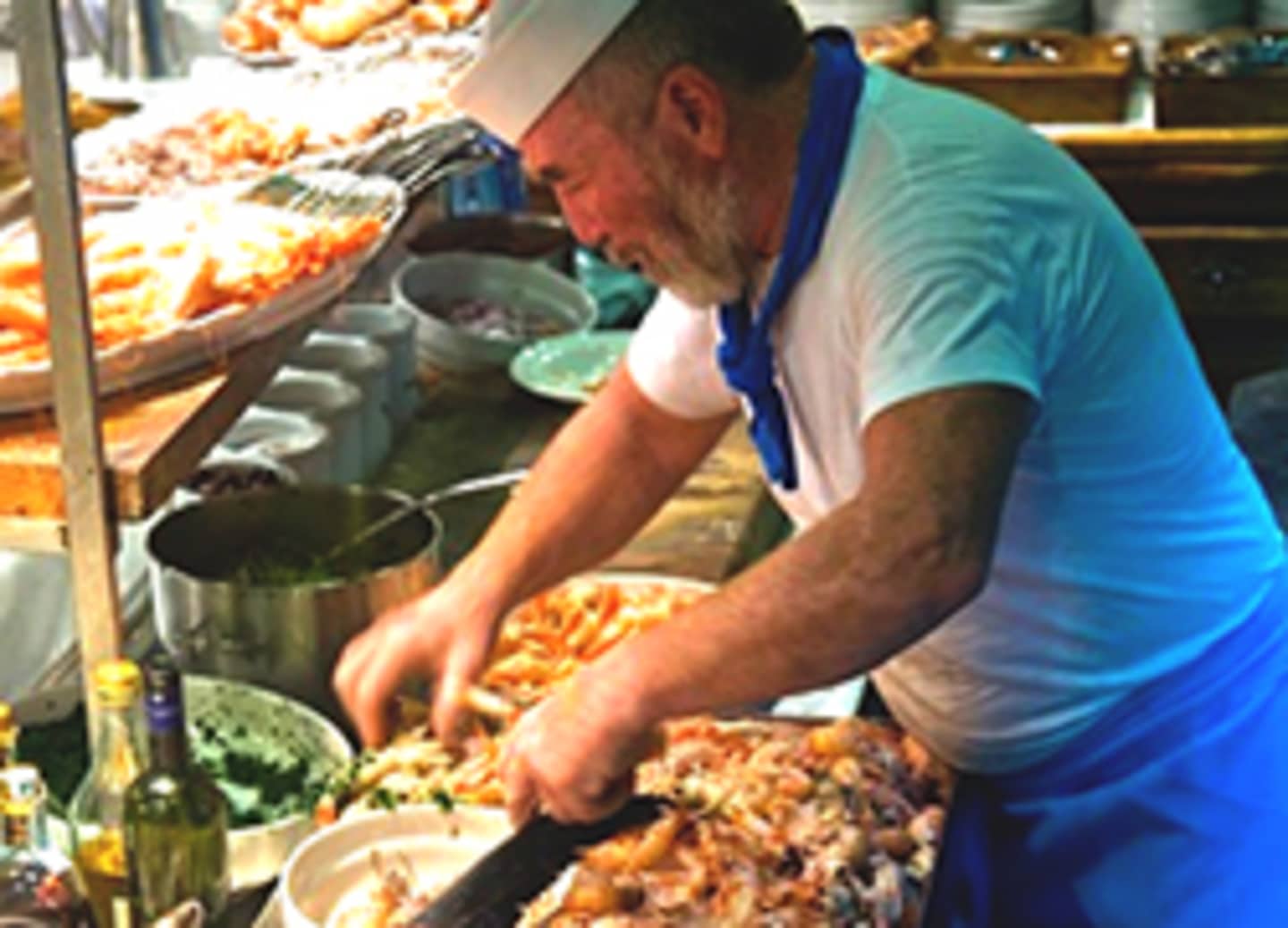 A man in a blue shirt is preparing food in a kitchen setting, surrounded by various ingredients and cooking equipment.