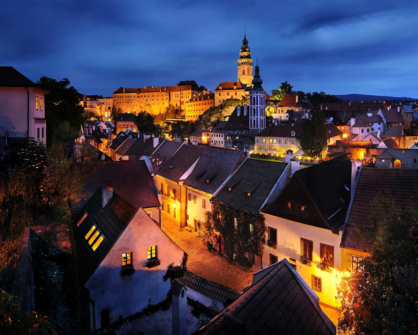 A picturesque medieval town nestled in a valley, with a towering church steeple illuminating the night sky and the cozy houses below bathed in a warm glow.