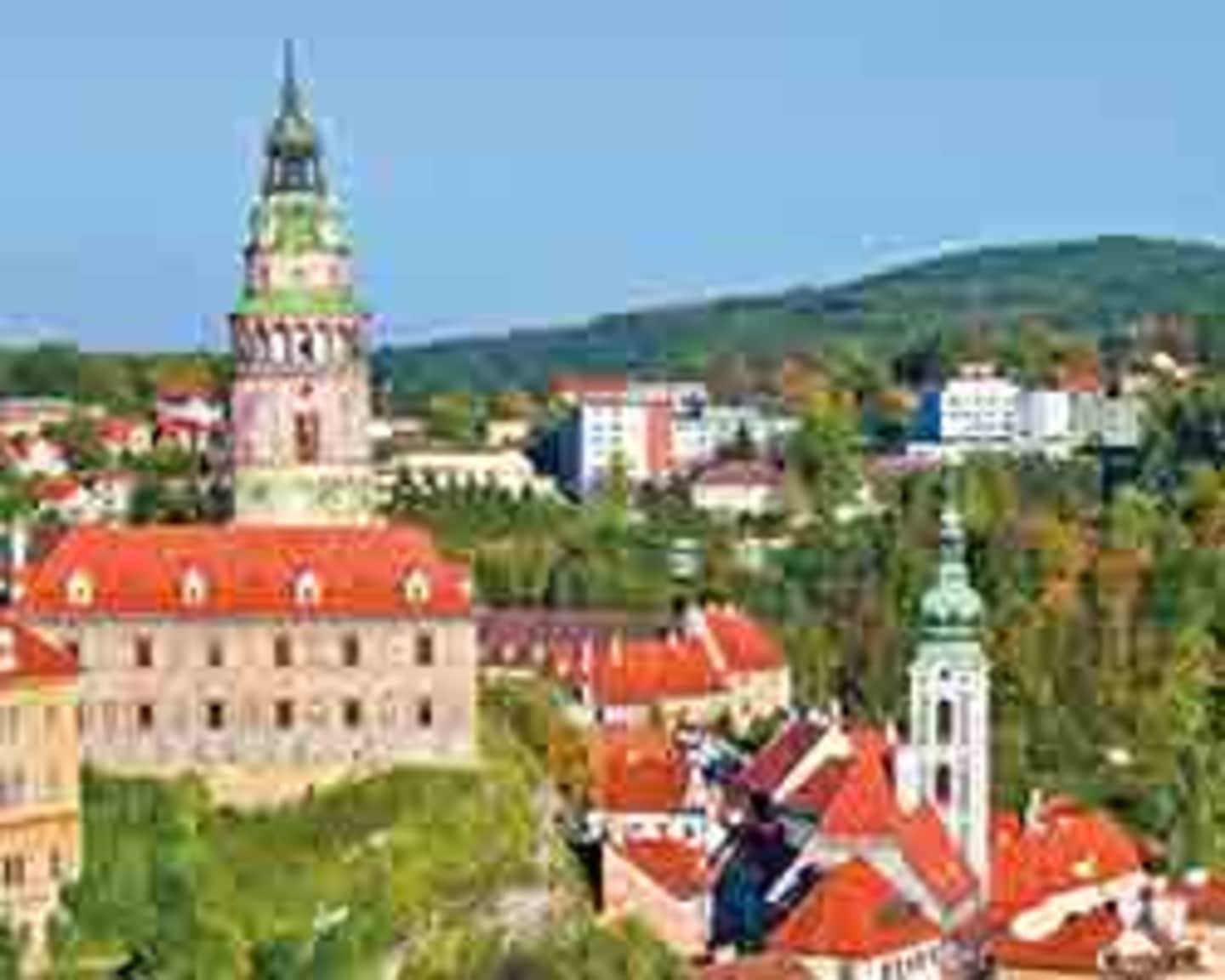 A picturesque town nestled in a lush, hilly landscape, with colorful rooftops, church spires, and a striking tower rising above the buildings.