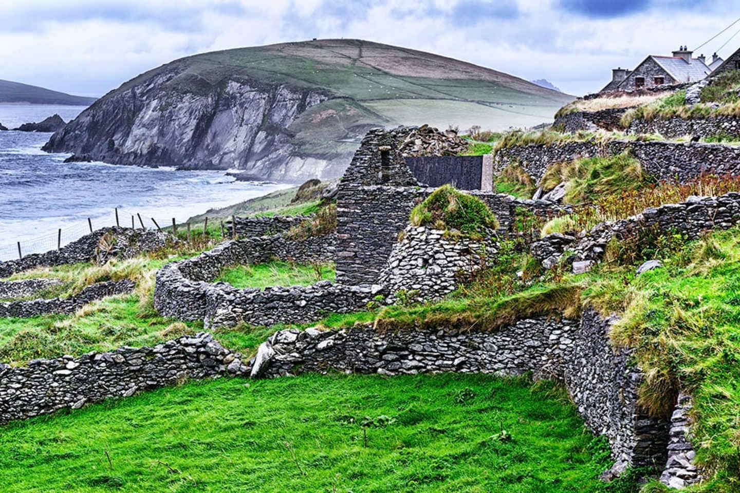 A rugged coastal landscape with stone walls and buildings nestled among the rolling hills, overlooking the vast expanse of the ocean and a towering cliff in the distance.