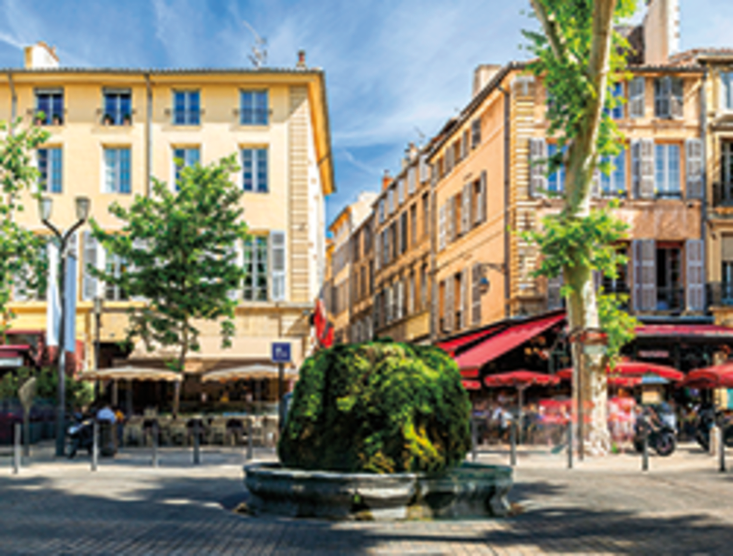 A quaint European city street with colorful buildings, outdoor cafes, and a decorative fountain in the foreground.