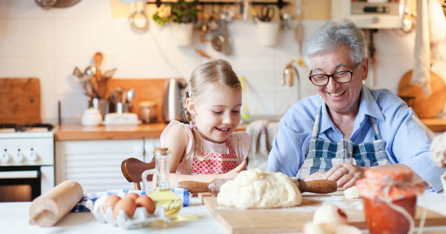 An elderly woman and a young girl are happily baking together in a cozy kitchen filled with cooking utensils and appliances.