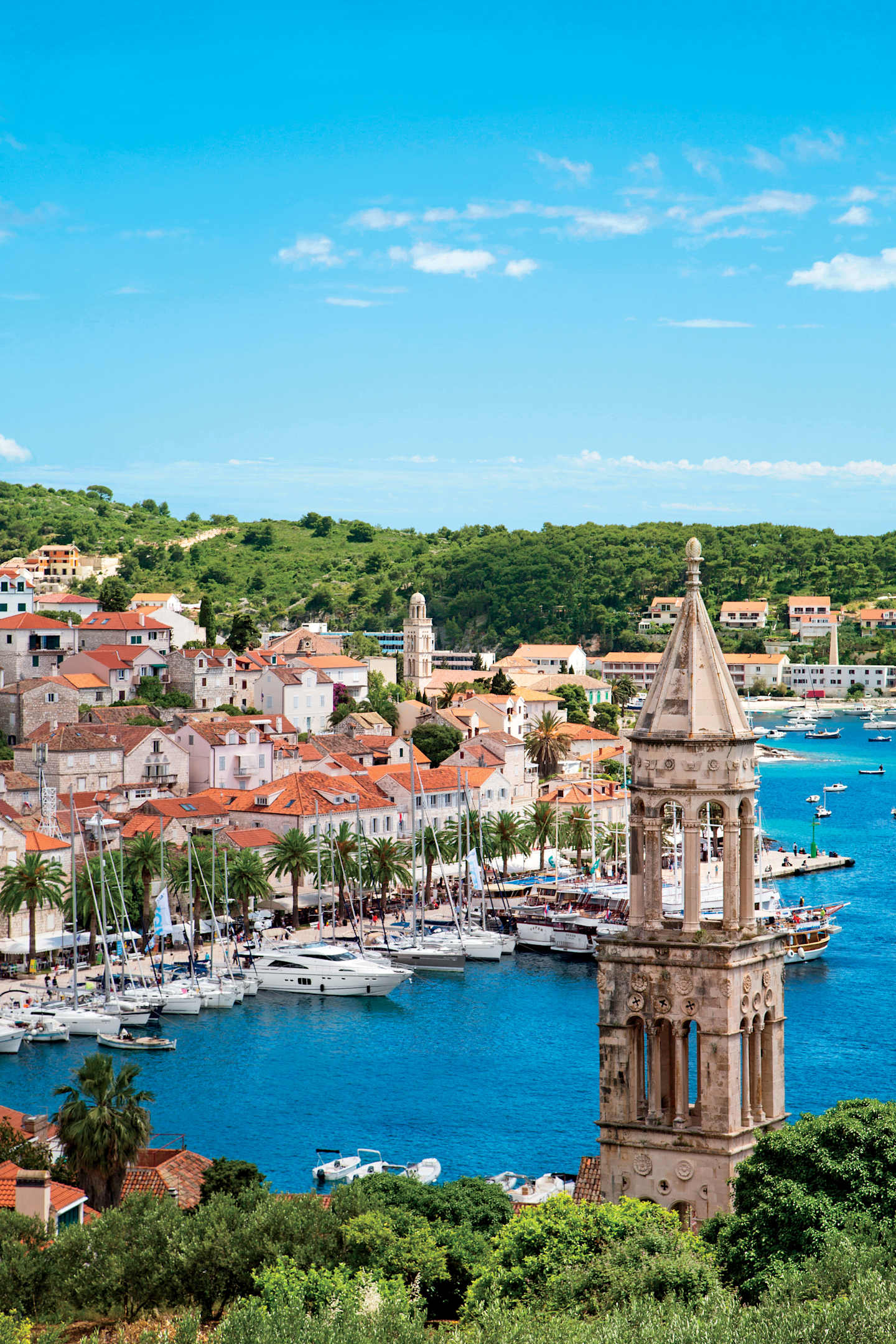 A picturesque coastal town with colorful buildings, a harbor filled with boats, and a towering church steeple overlooking the serene blue waters of the Mediterranean Sea.