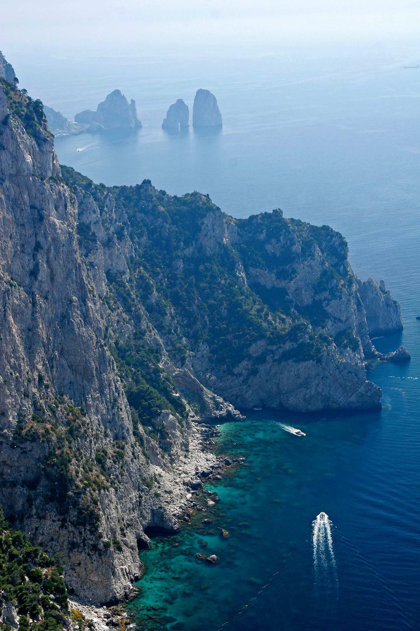 A rugged, mountainous coastline with towering cliffs overlooking a serene, turquoise sea dotted with small islands in the distance.