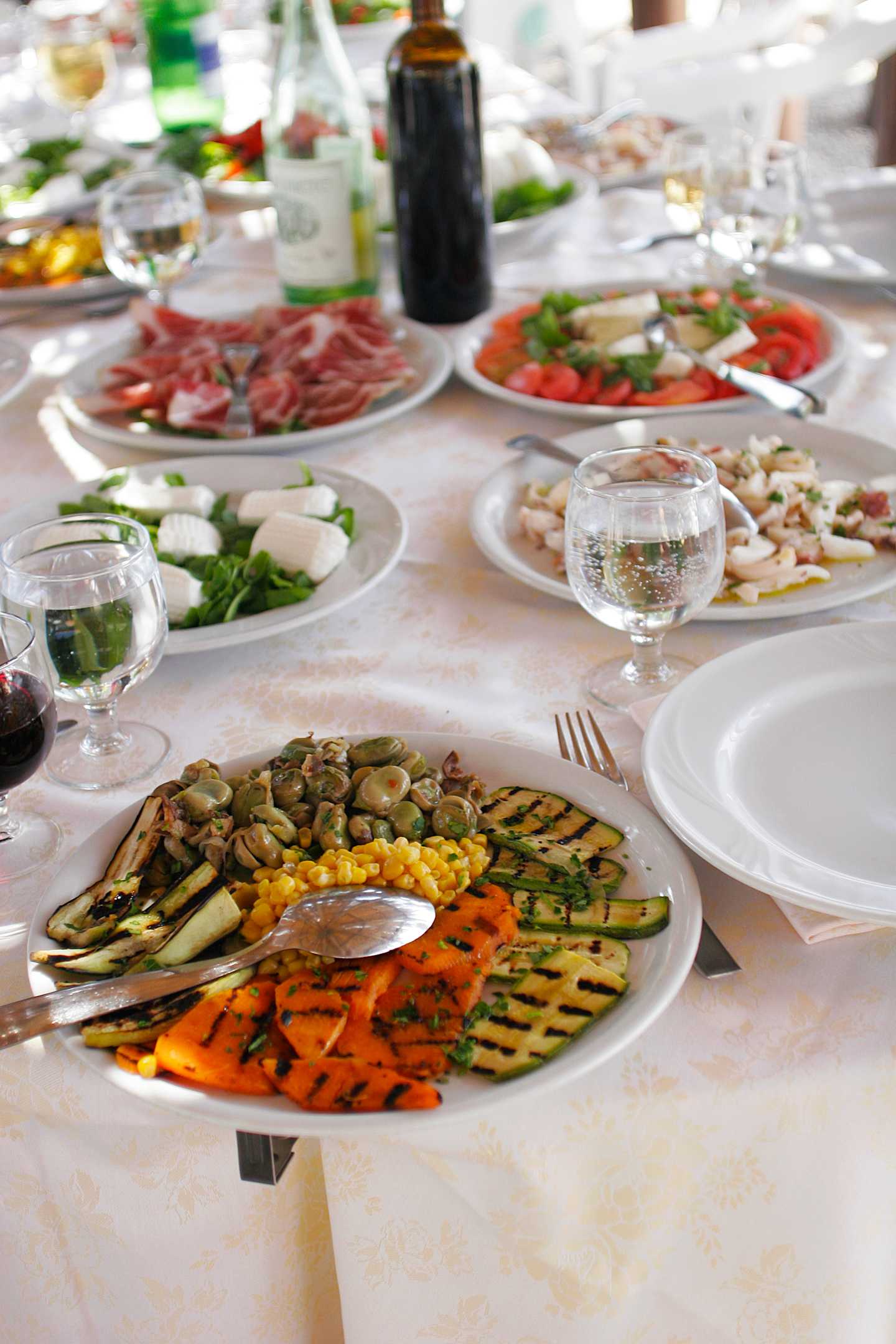 A table filled with a variety of appetizing dishes, including grilled vegetables, cured meats, and various salads, accompanied by glasses of wine, creating a visually appealing and inviting dining experience.