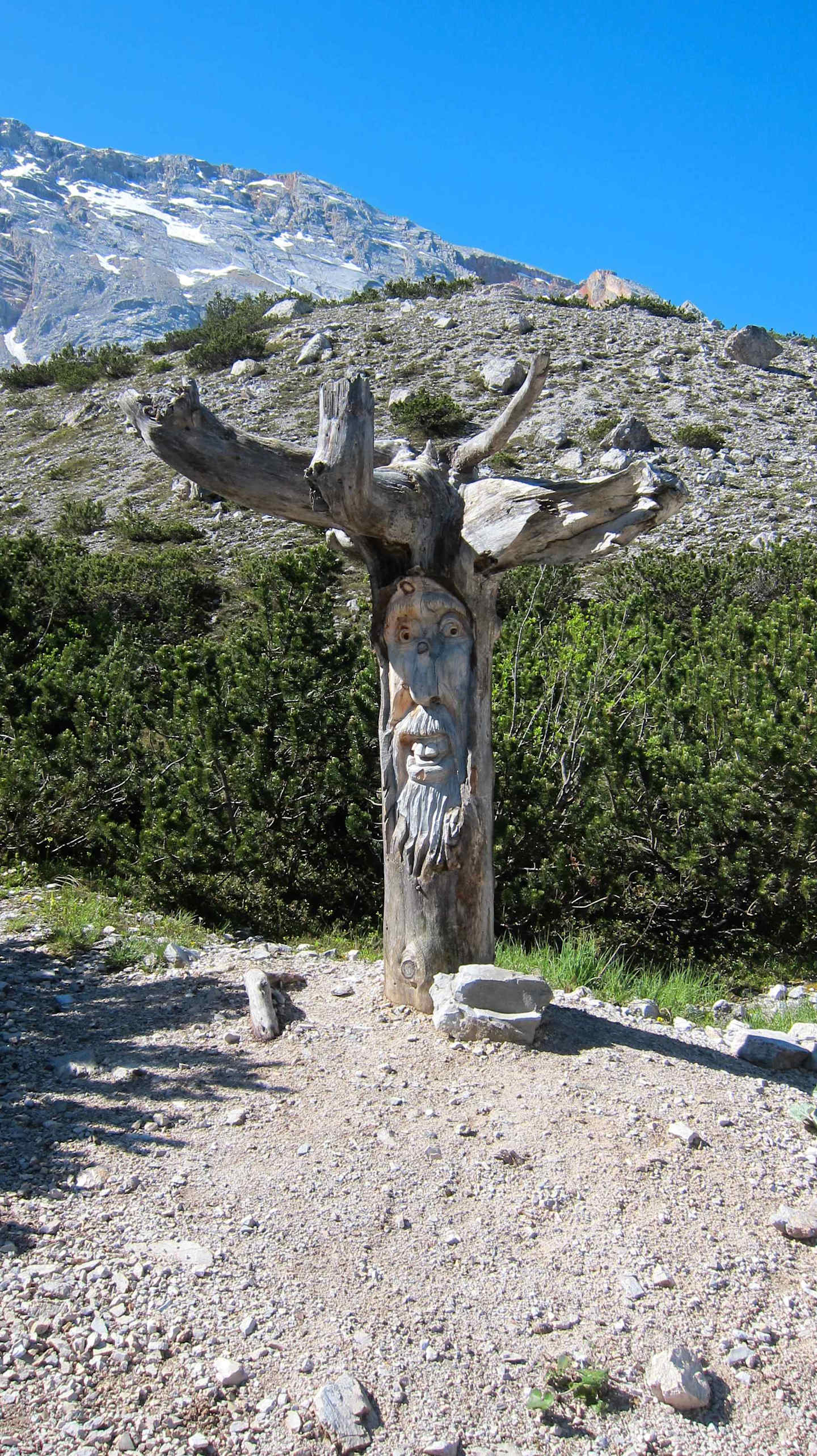 A large wooden sculpture of a deer or stag stands in the foreground, surrounded by a rocky, mountainous landscape in the background.