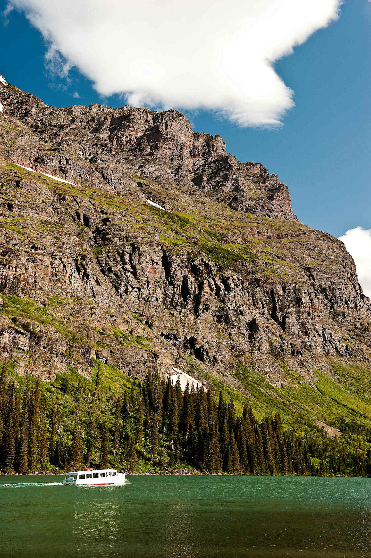 A scenic landscape with a serene green lake surrounded by rugged, snow-capped mountains and a forested area in the foreground.