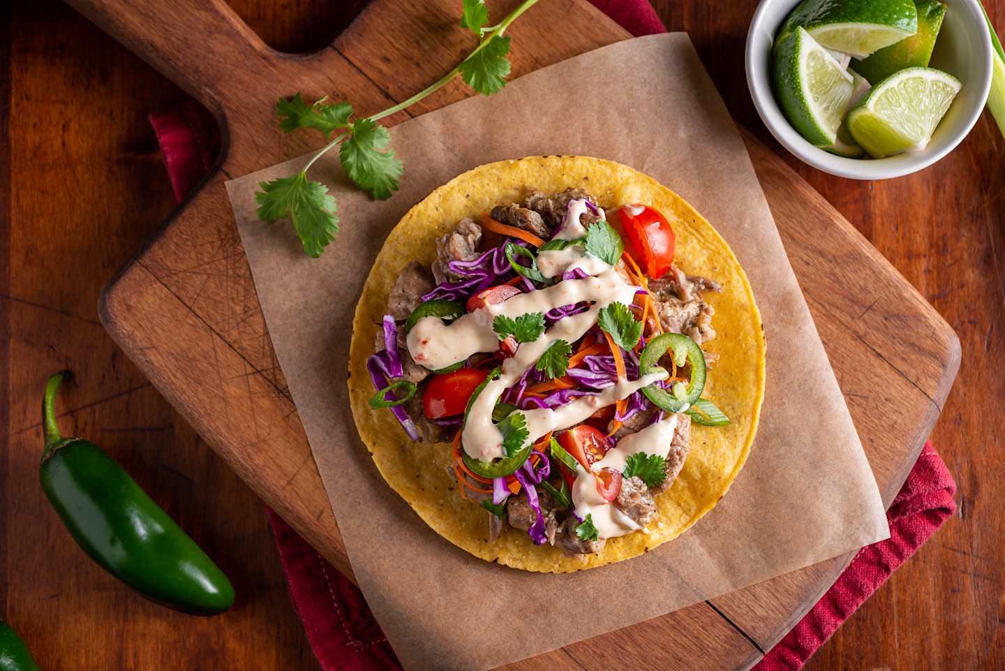A delicious-looking taco filled with a colorful mix of vegetables, meat, and garnishes, resting on a wooden cutting board alongside fresh limes and other ingredients.