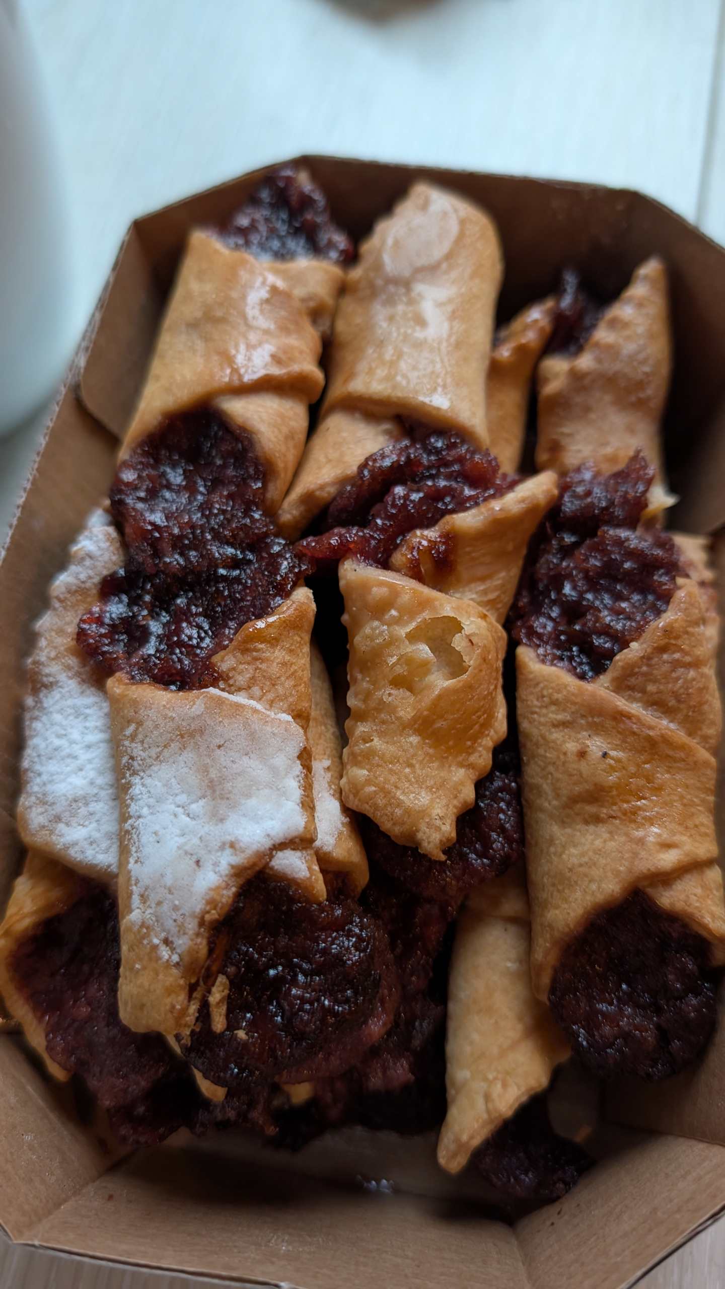 The image shows a plate filled with various pastries, including what appears to be flaky, golden-brown croissants or similar baked goods, along with a dark, jam-like filling or topping that has been spread across the surface of the pastries.