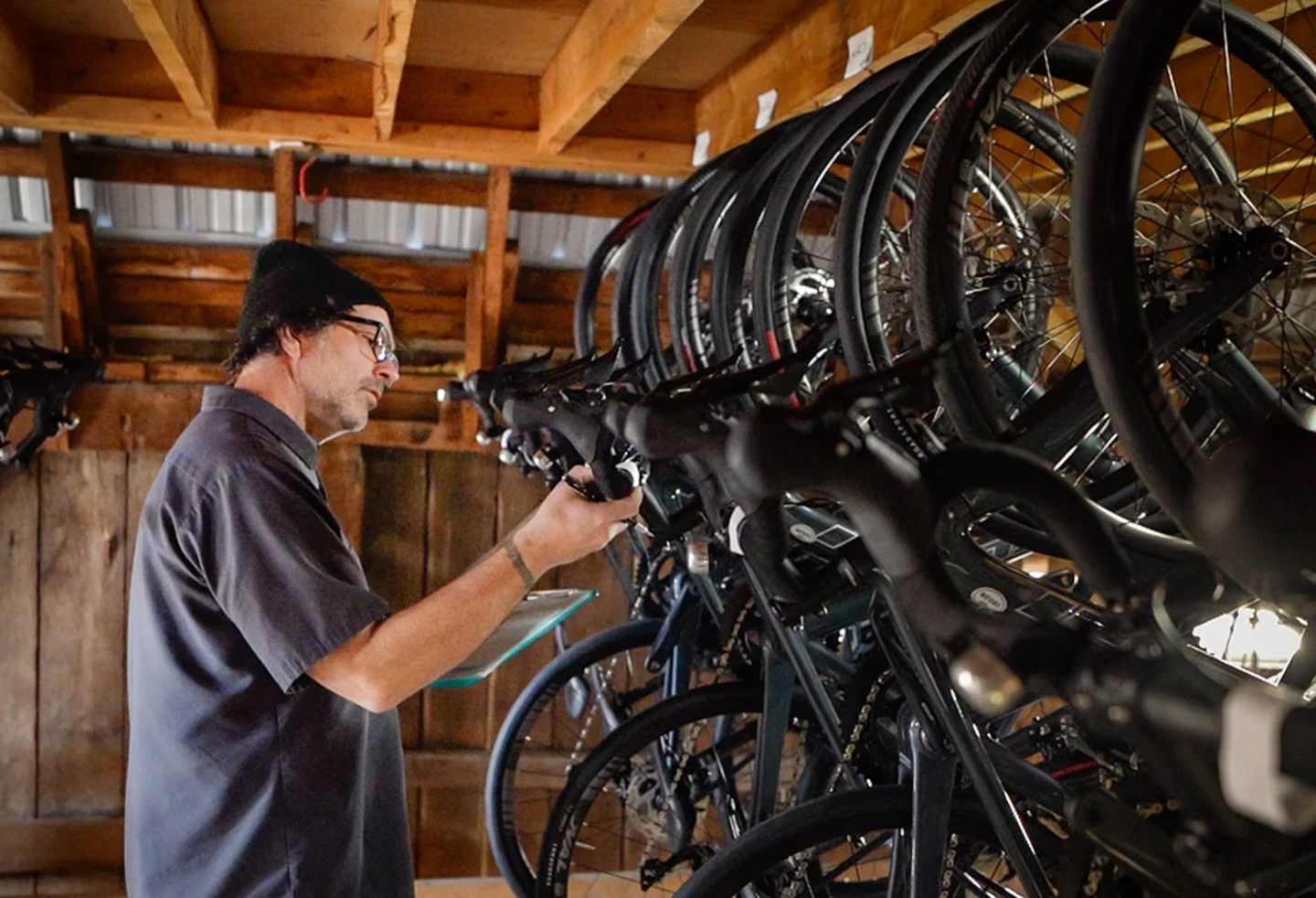 A person in a dark shirt is working on a row of bicycles in a wooden shed or garage.