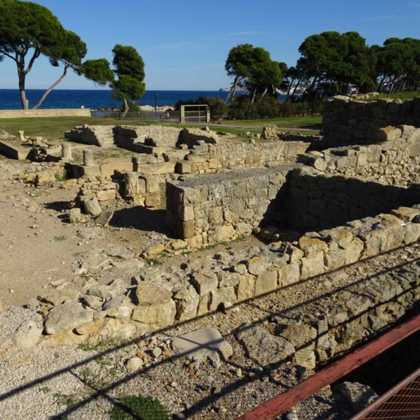 Weathered stone ruins surrounded by lush greenery and a tranquil blue sea in the background.