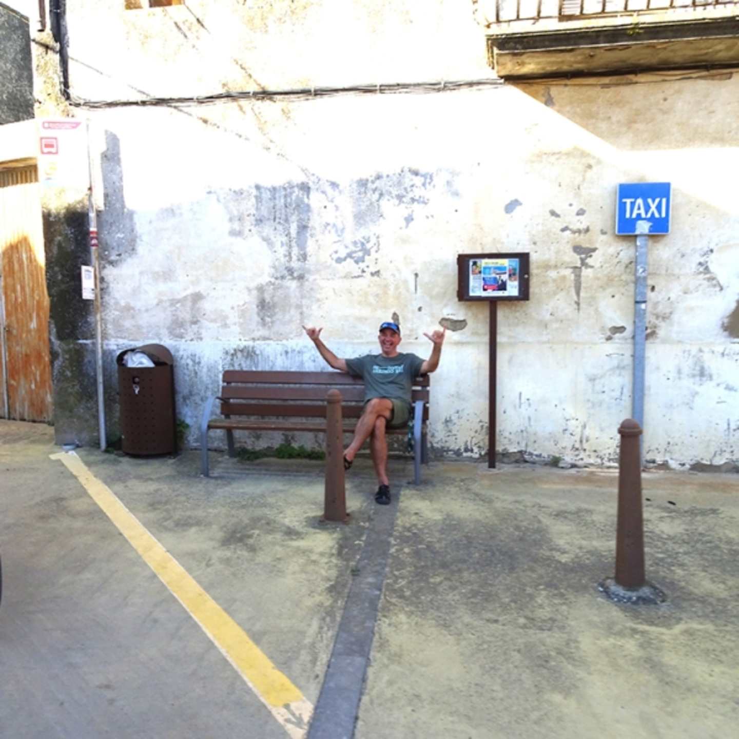A person is sitting on a bench in a dilapidated urban setting, with a taxi sign and other elements in the background.