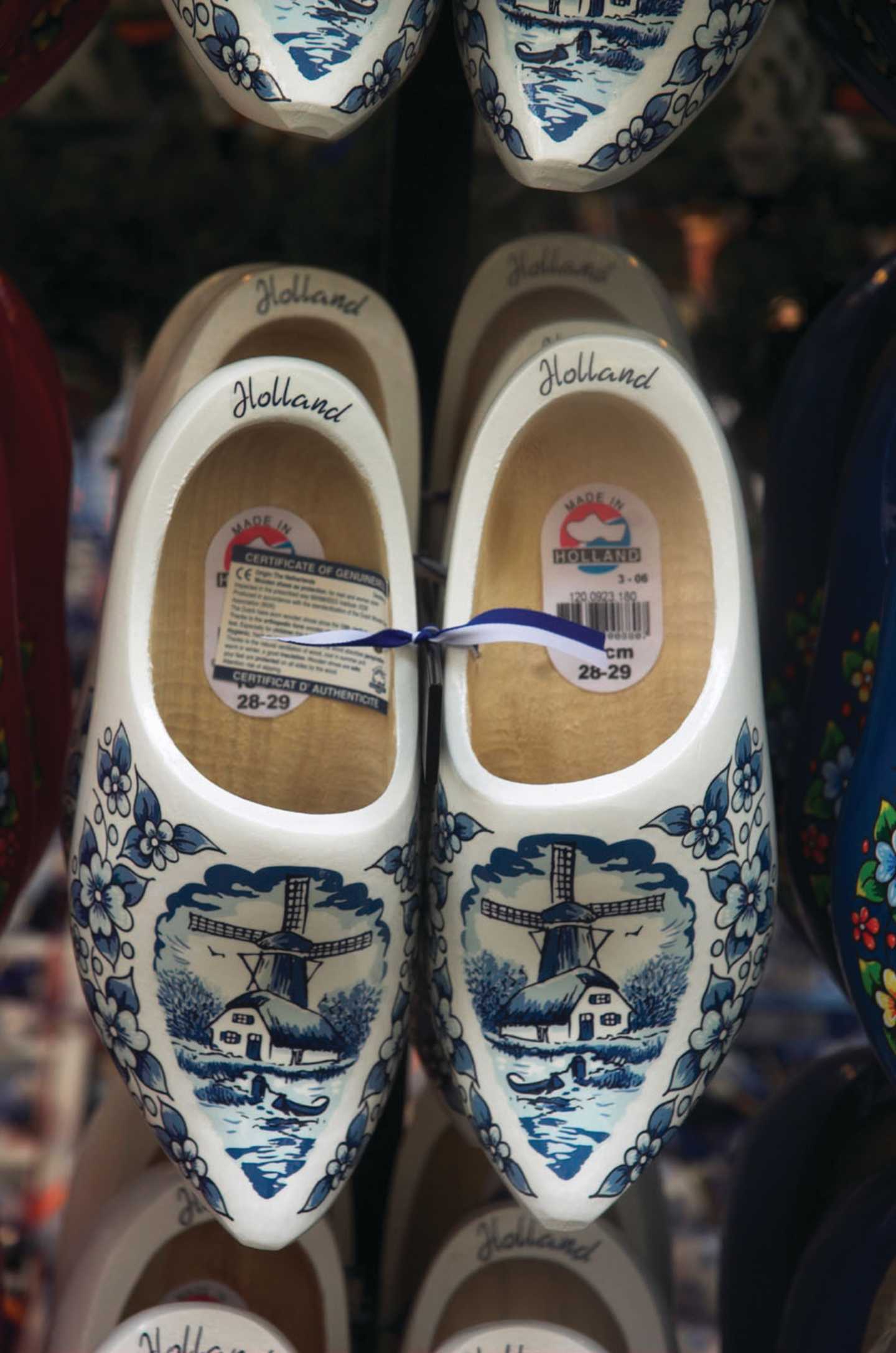 The image shows a pair of traditional Dutch wooden clogs or "klompen" decorated with a blue and white landscape pattern, including windmills and houses.