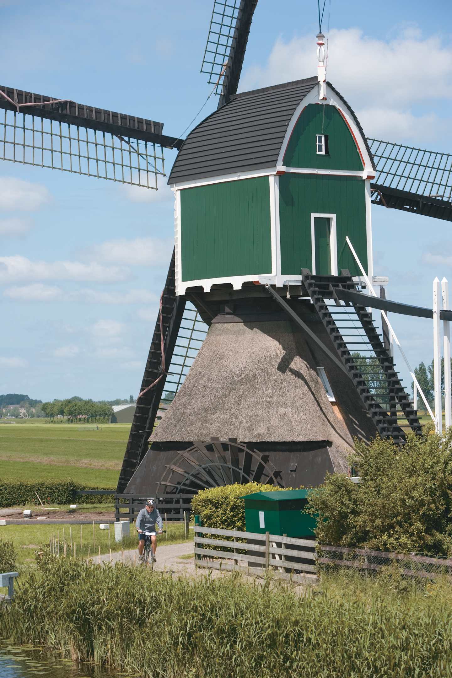 A traditional Dutch windmill stands prominently in the foreground, surrounded by a grassy field and a cyclist riding in the distance.