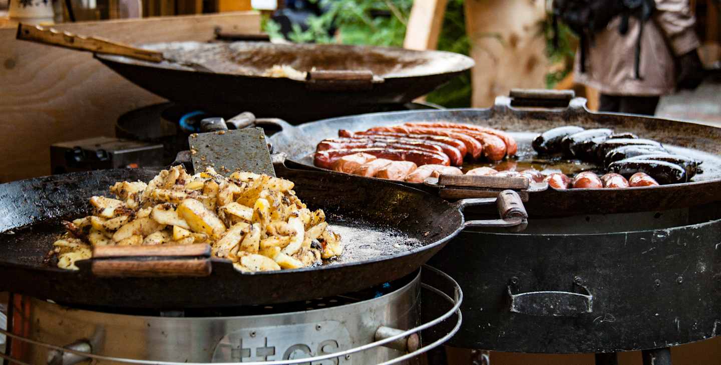 A cast iron pan filled with sizzling fries, alongside a platter of grilled sausages and other meats, set against a rustic wooden background.