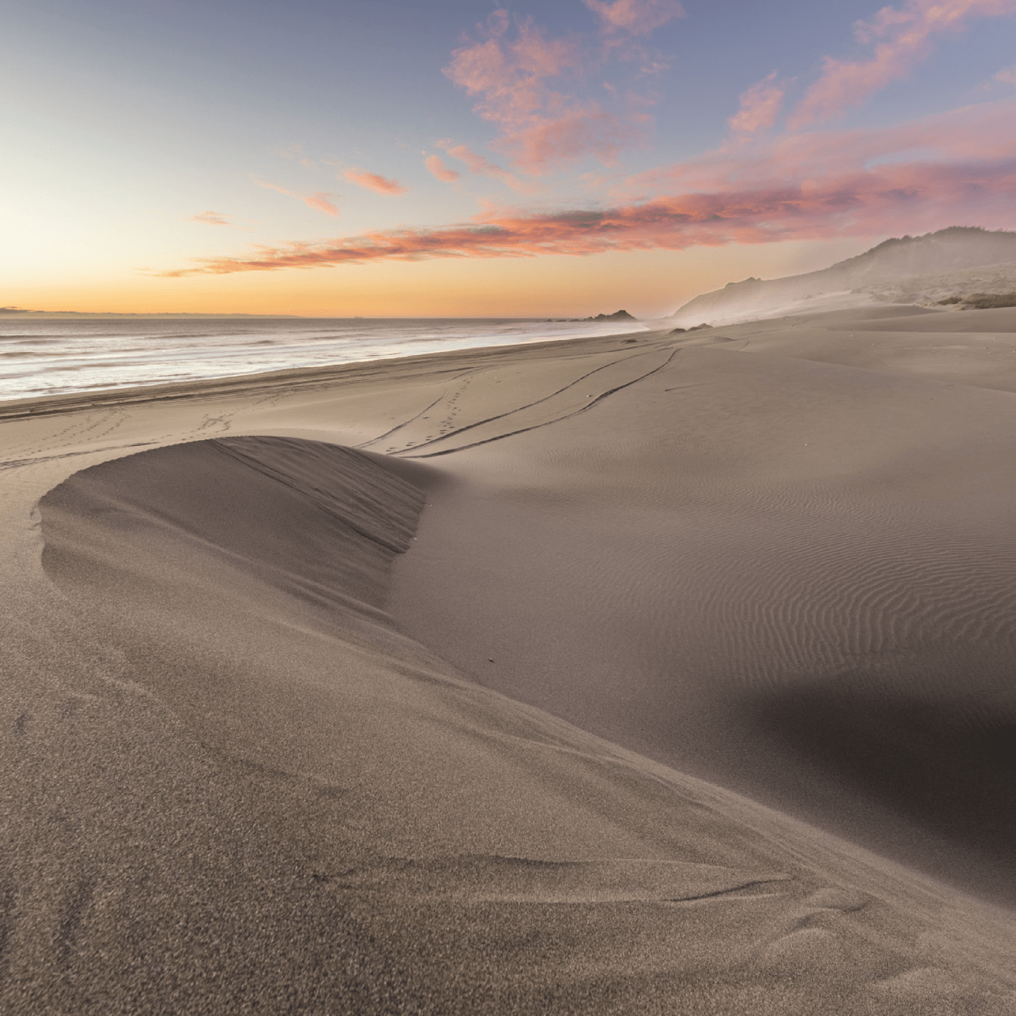 A scenic rural landscape with a paved road, vineyards, and mountains in the background, with two people cycling in the distance.