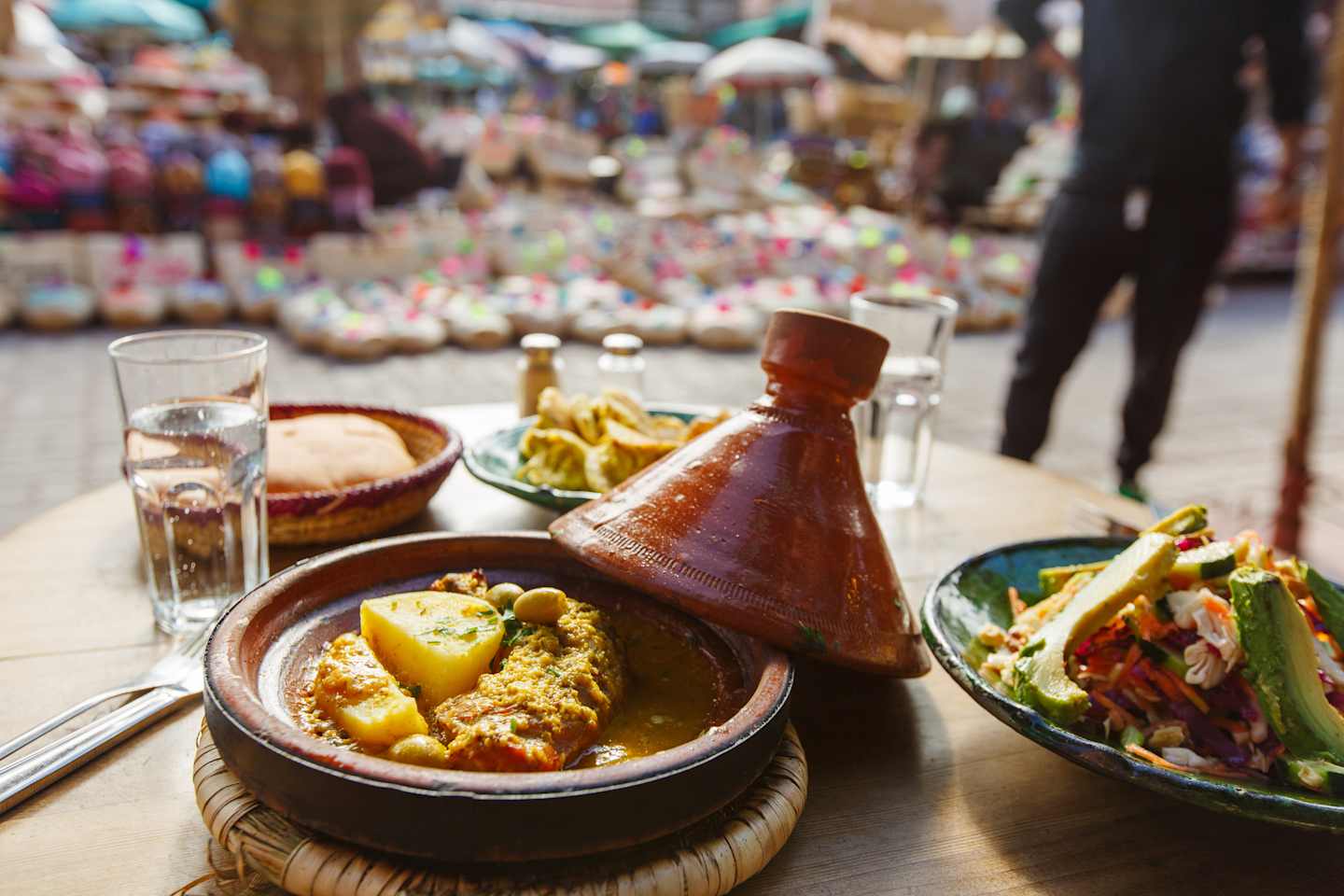 A traditional Moroccan dish, featuring a tagine pot filled with a savory stew, accompanied by a fresh salad and other side dishes, set against the vibrant backdrop of a bustling market scene.