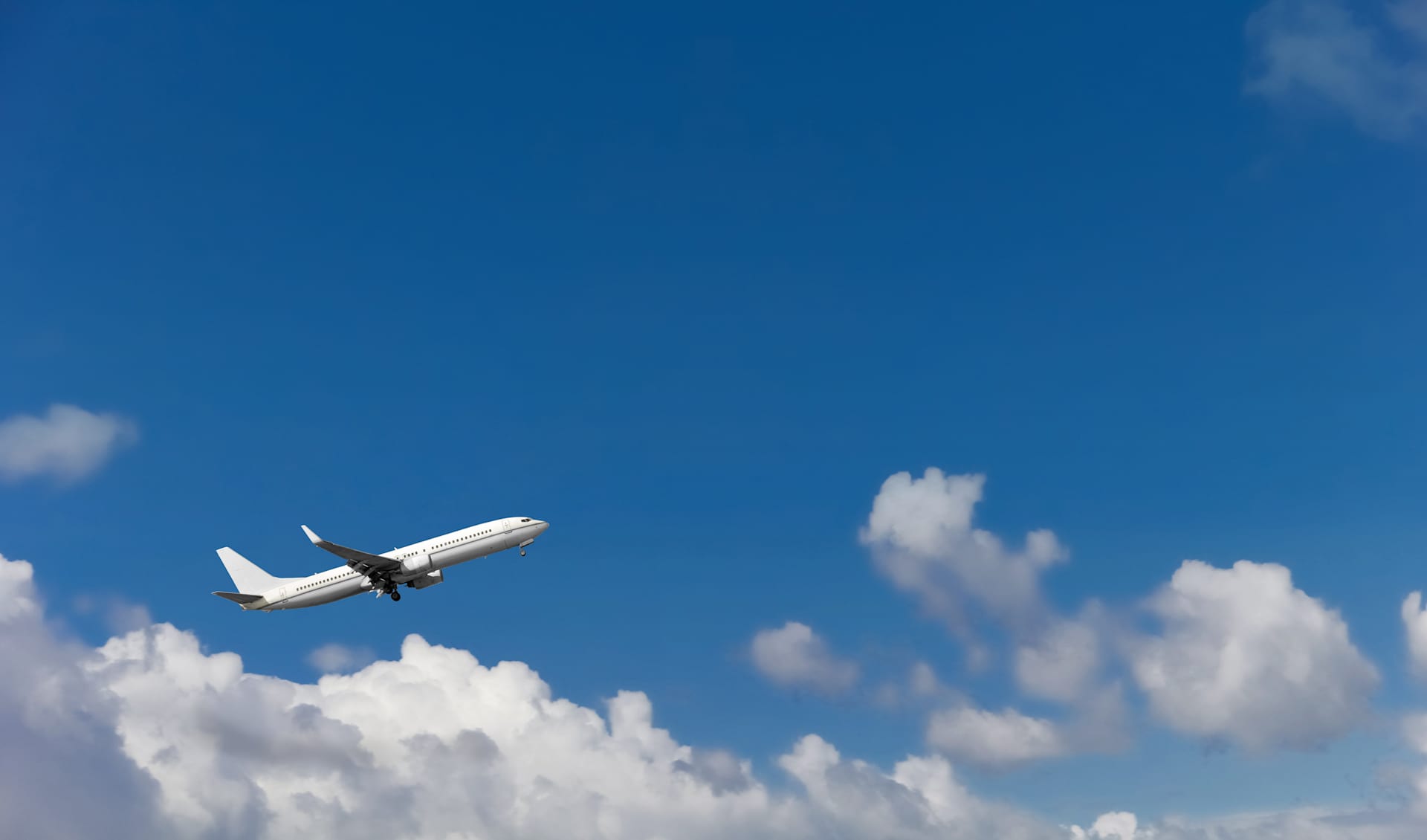A commercial passenger airplane soars through the bright blue sky, surrounded by fluffy white clouds.