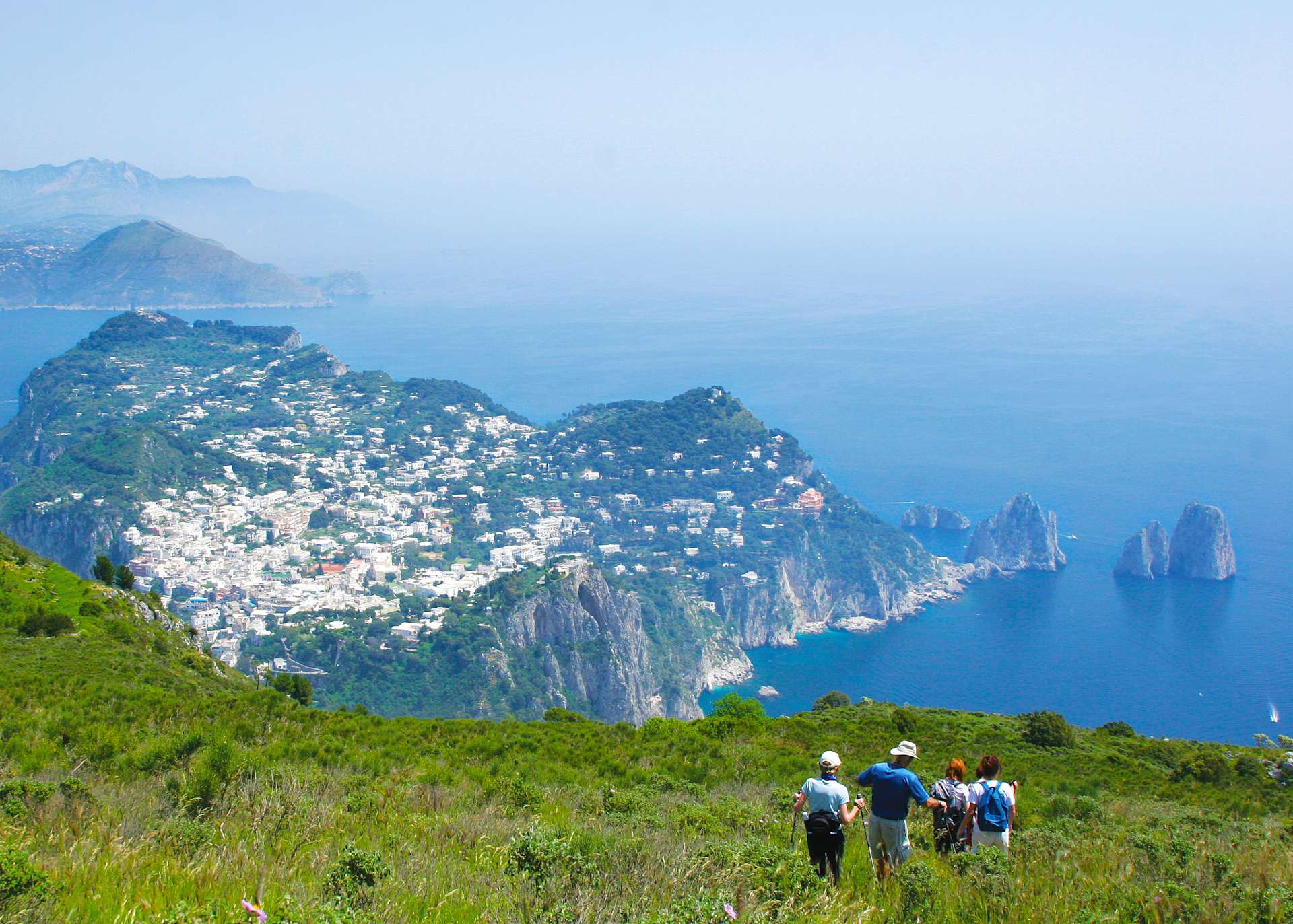 A scenic coastal town nestled among rugged cliffs and mountains, with a group of hikers enjoying the breathtaking view in the foreground.