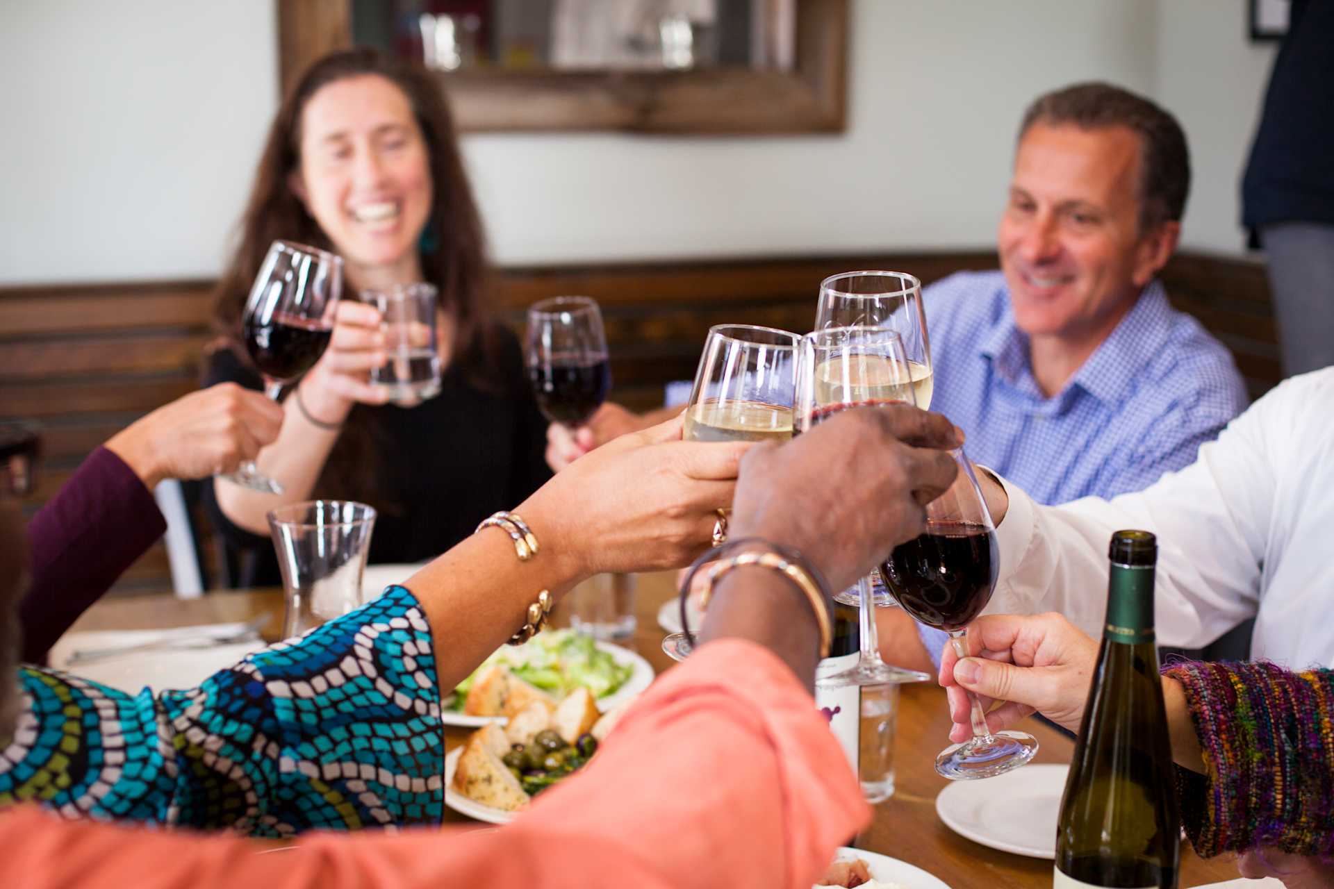 A group of people are gathered around a table, enjoying a meal and drinks together, with a cozy and intimate atmosphere in the background.