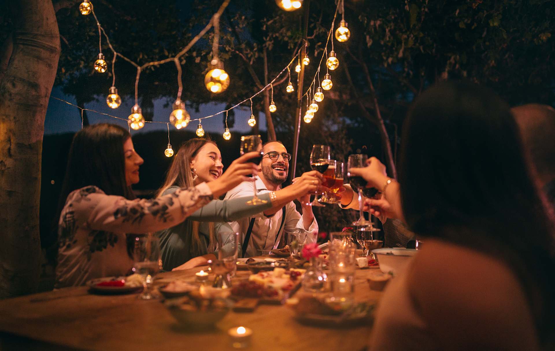 A group of people enjoying a festive outdoor dinner party, surrounded by twinkling string lights and a cozy, intimate atmosphere.