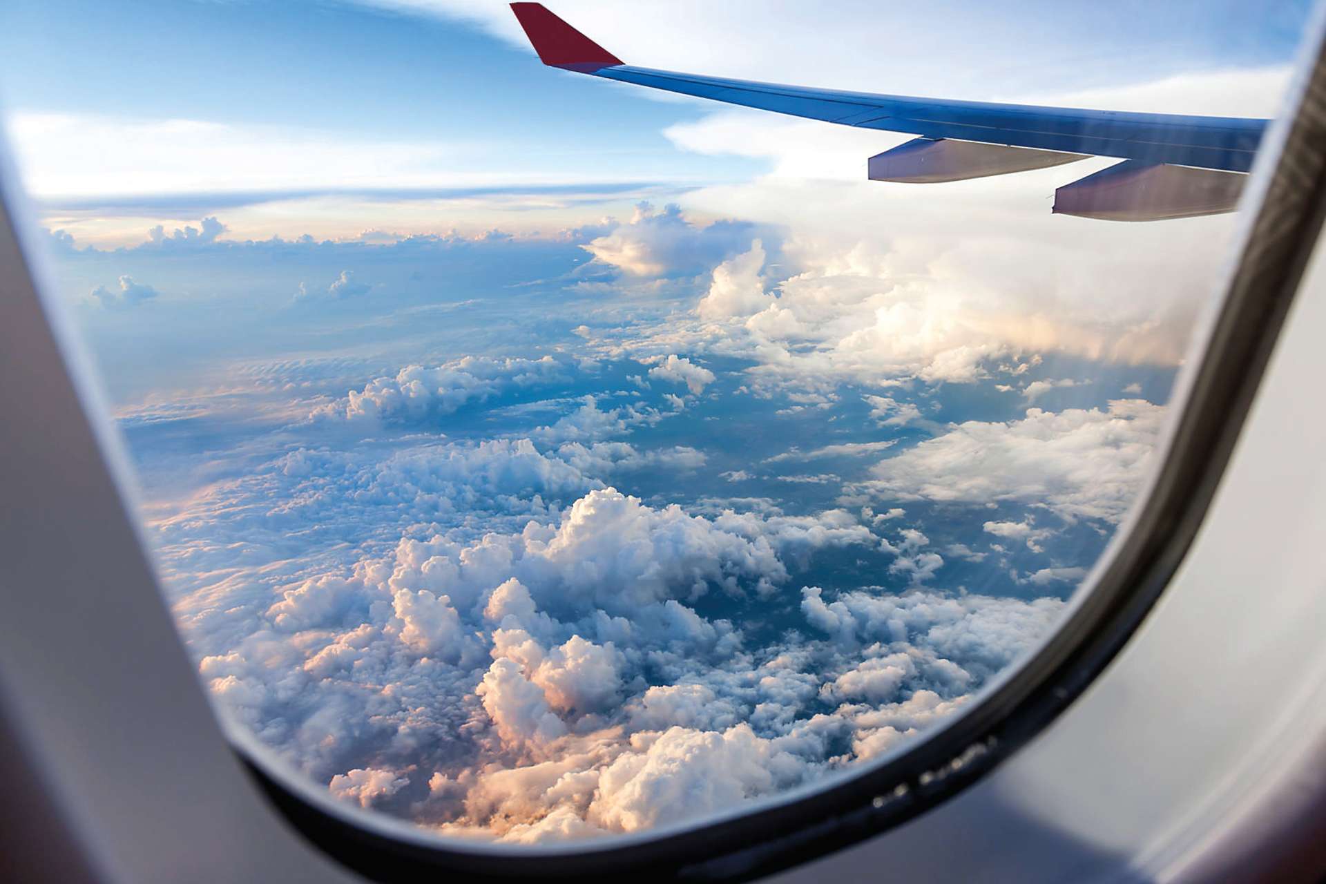 The image shows the wing of an aircraft with a red and blue color scheme, and the background is filled with a vast expanse of clouds and sky, creating a serene and picturesque aerial view.
