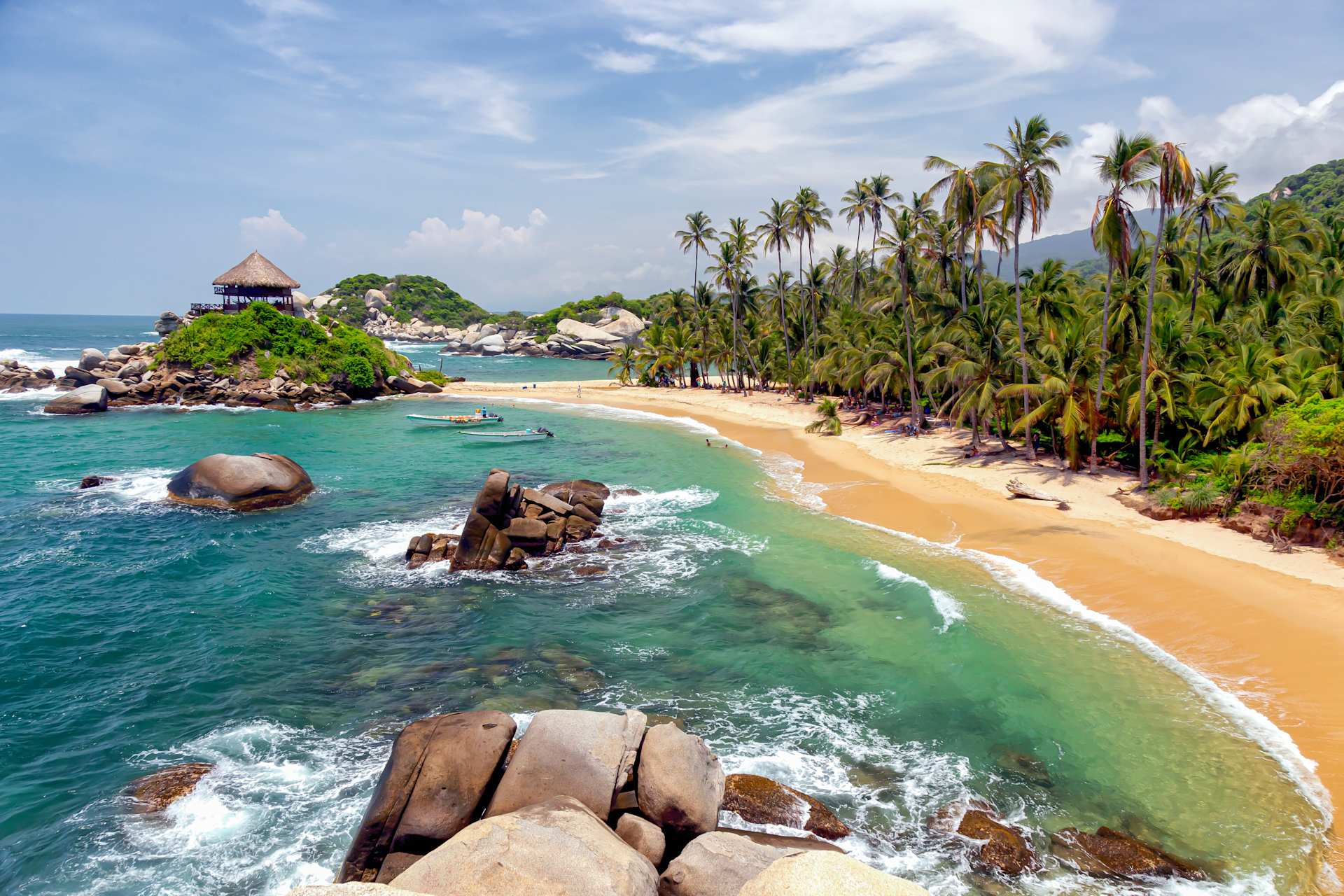 A picturesque tropical beach with palm trees, rocky outcroppings, and crystal-clear turquoise waters lapping against the golden sand.