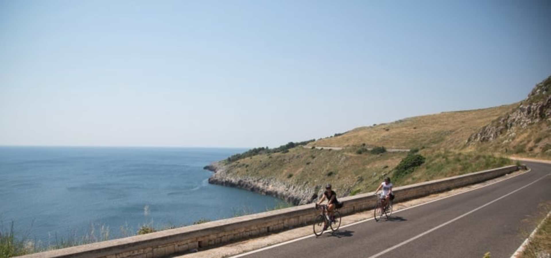 A scenic coastal road with cyclists riding along the edge of a cliff overlooking the vast, blue ocean.