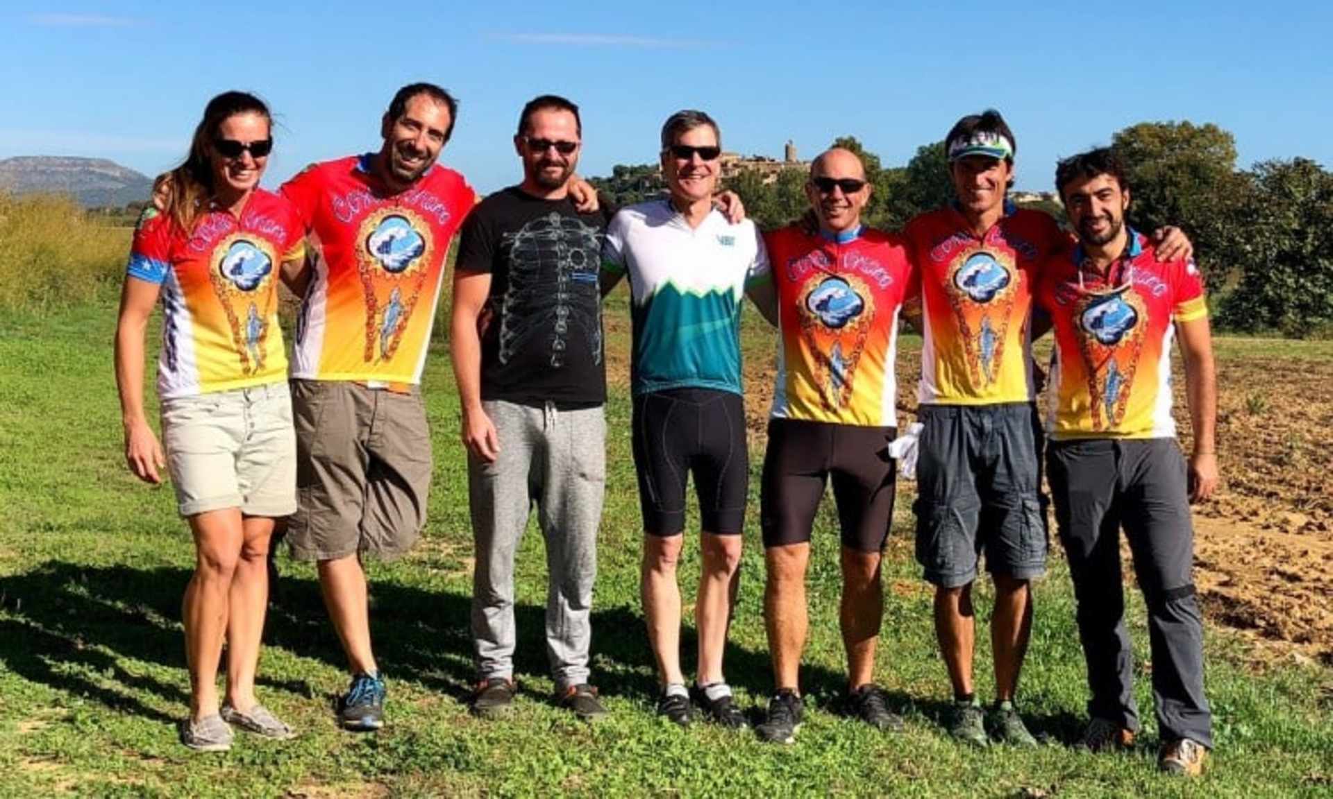 A group of people wearing colorful jerseys stands together in a grassy field with mountains visible in the background.