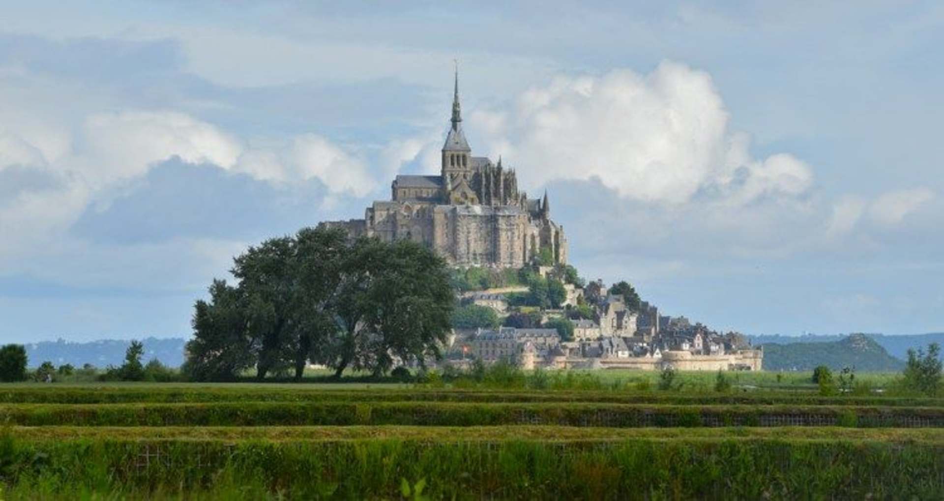 A majestic castle-like structure stands atop a hill, surrounded by lush greenery and a scenic landscape in the foreground.