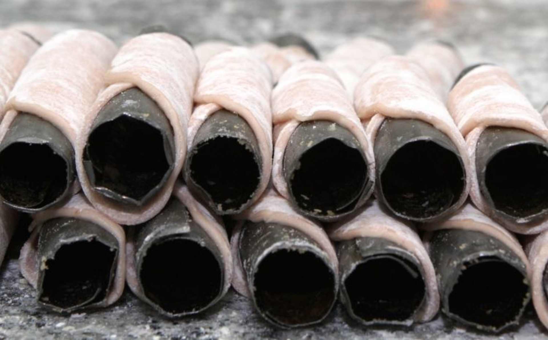 The image shows a close-up view of several cylindrical, hollow structures with a pale, pinkish-white exterior and a dark, empty interior. The structures appear to be arranged in rows, suggesting they may be some type of industrial or manufacturing product.