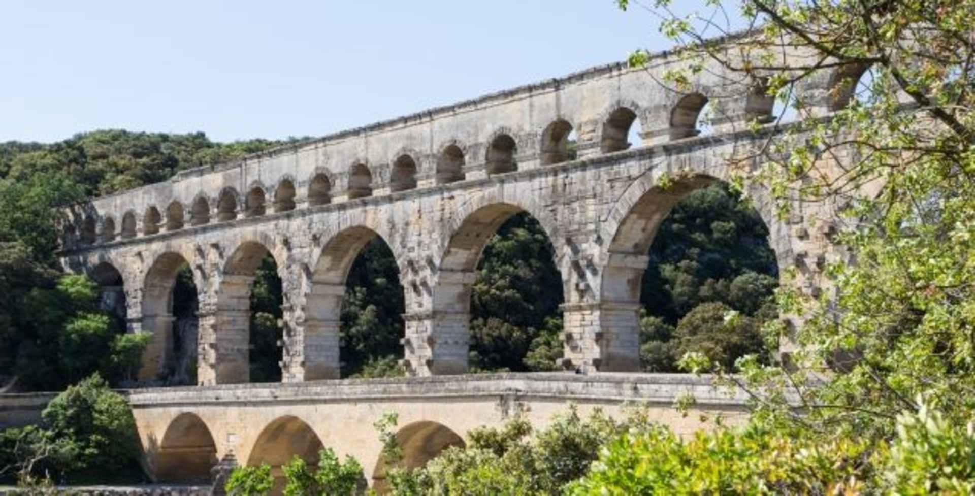 A majestic stone aqueduct with multiple arched spans stands amidst lush greenery, creating a striking architectural contrast against the natural backdrop.