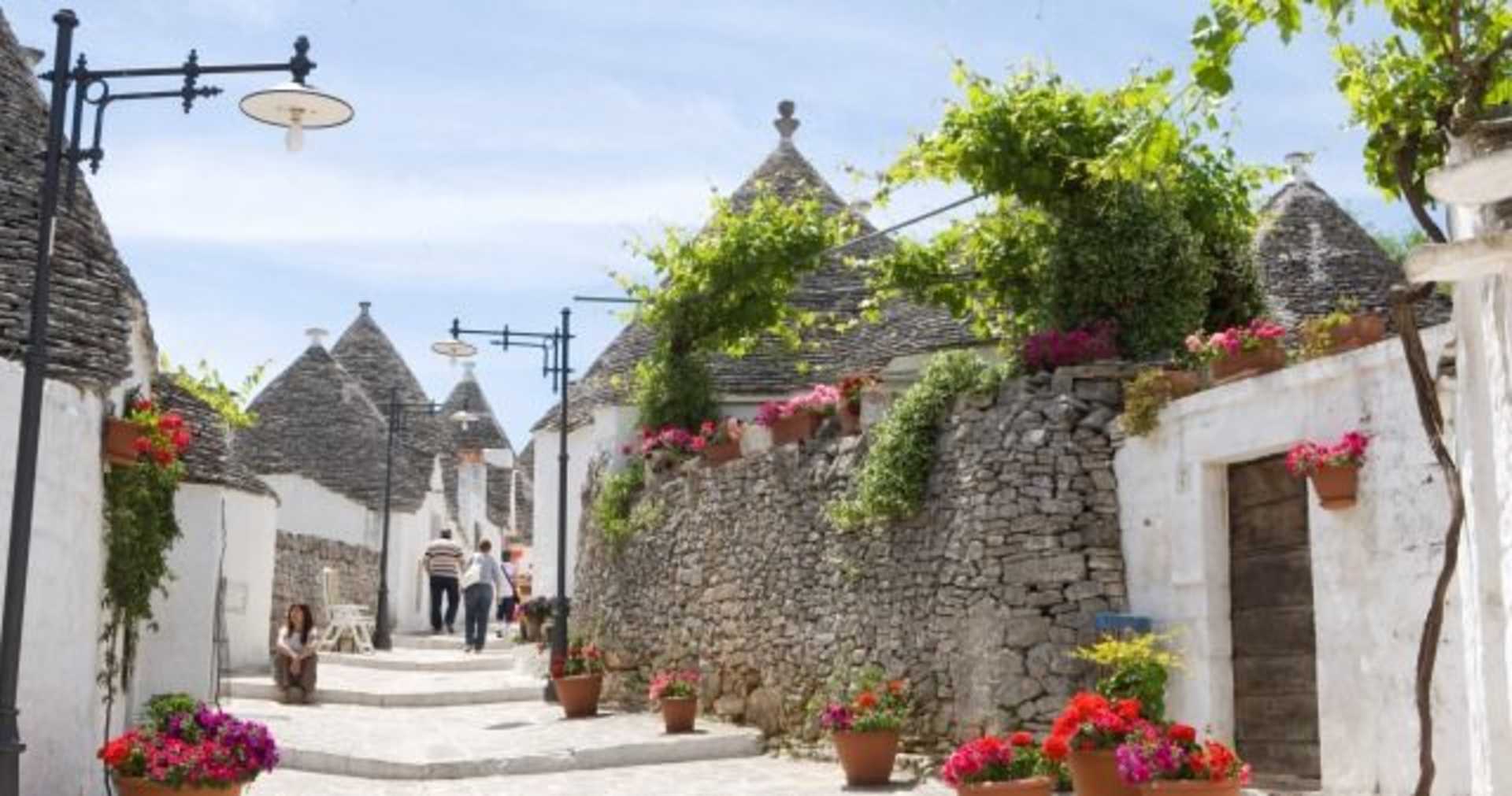 A picturesque alleyway lined with stone buildings, lush greenery, and colorful potted flowers, creating a charming and inviting atmosphere.