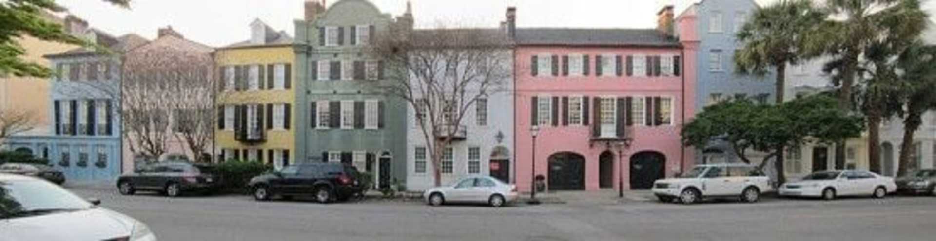 Colorful historic buildings line the street, with parked cars in the foreground and bare trees in the background.
