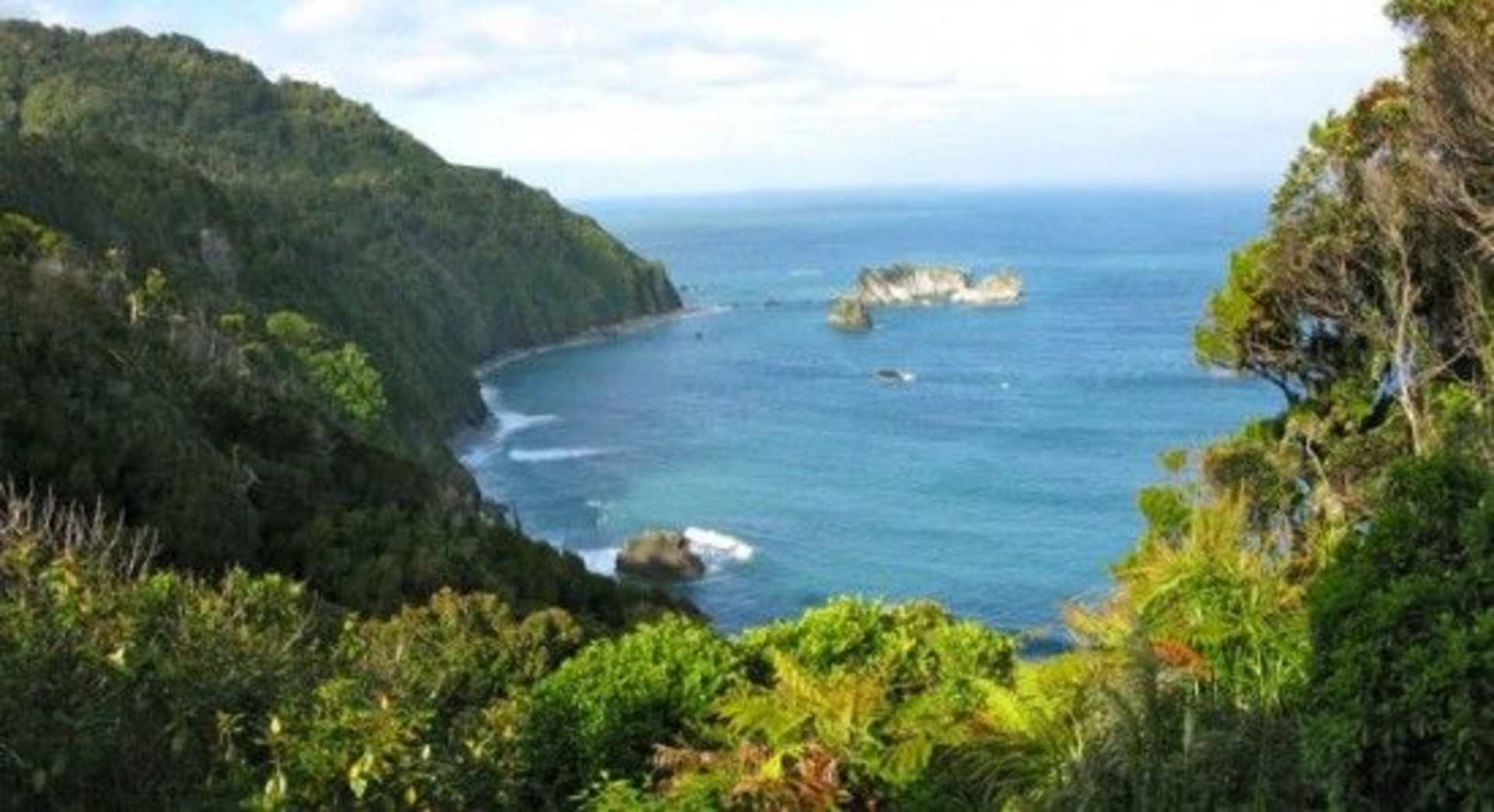 A lush, verdant landscape with towering cliffs overlooking a vibrant, turquoise sea dotted with rocky outcroppings in the distance.