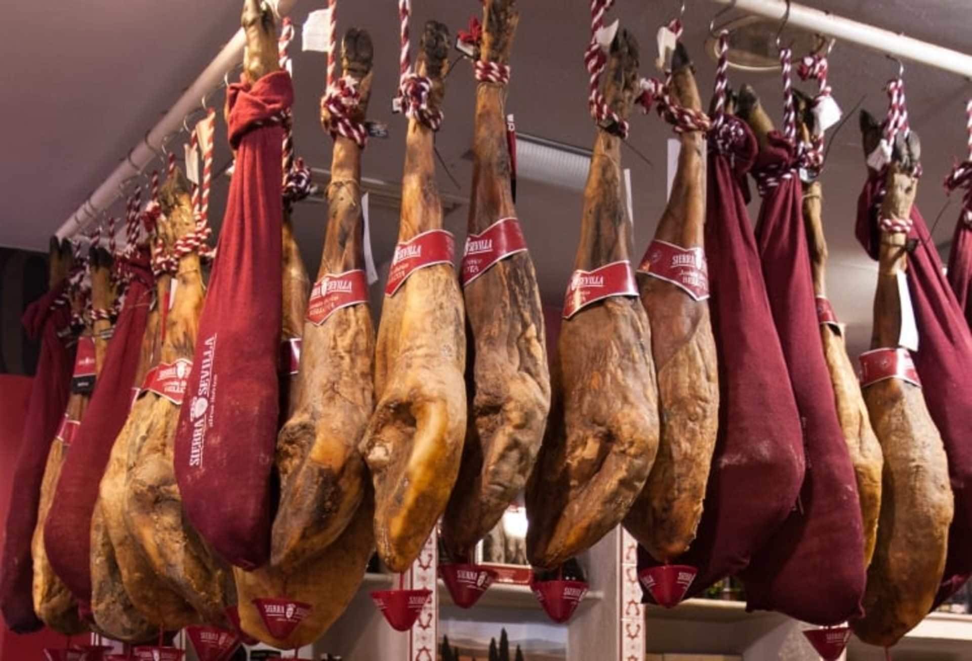 The image shows a display of various cured and smoked meat products, including hams and sausages, hanging from a rack in what appears to be a specialty food or butcher shop.