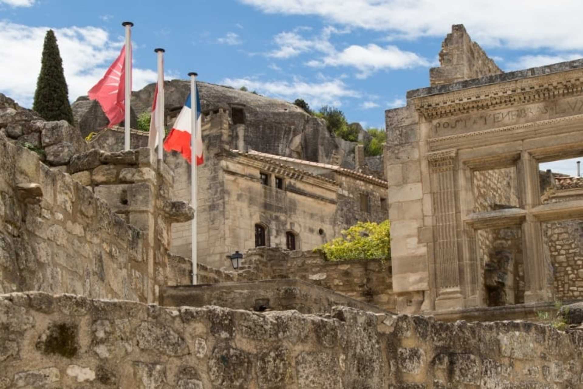 Majestic stone structures with flags flying atop, surrounded by ancient ruins and a clear blue sky with fluffy clouds.
