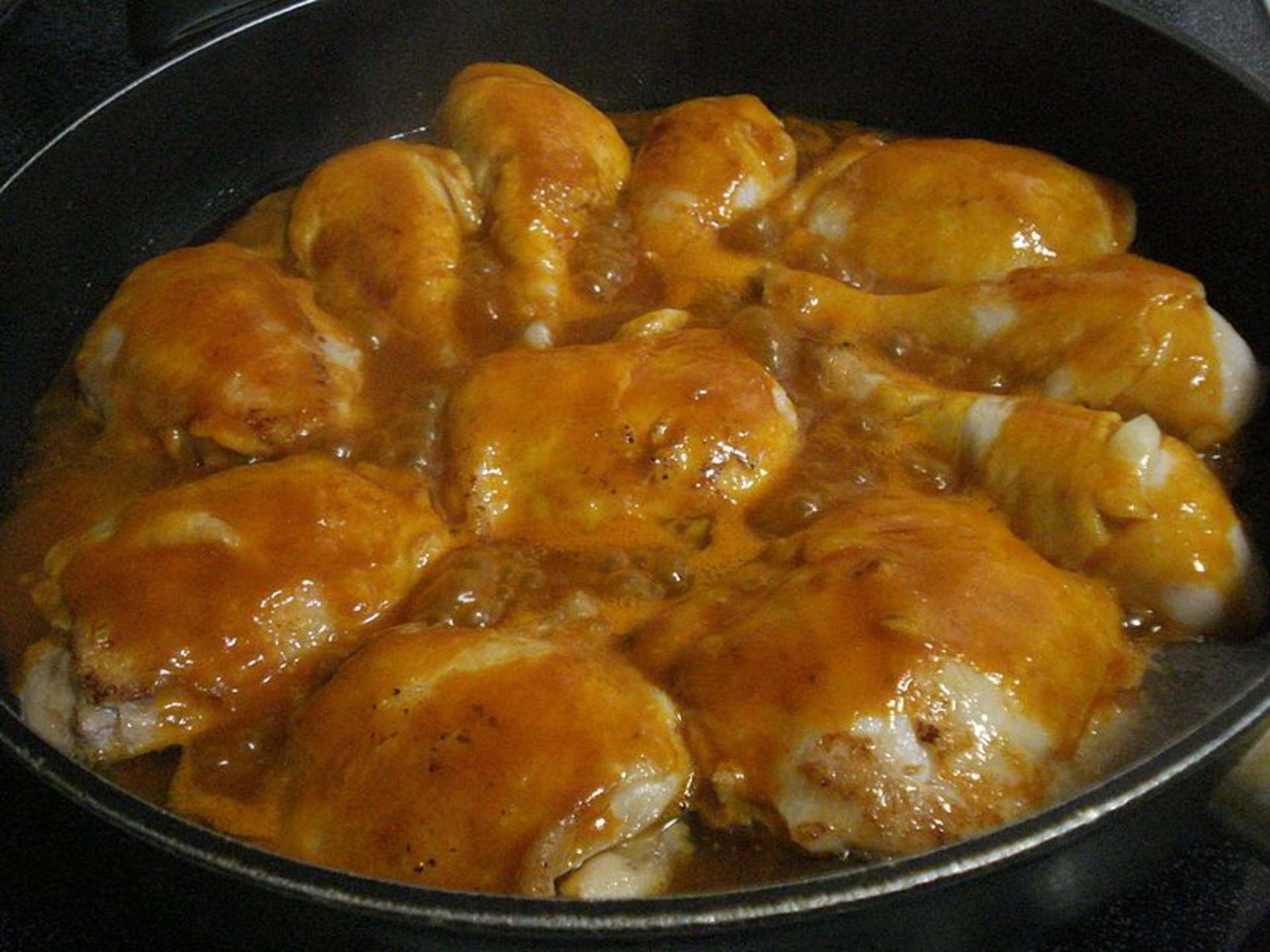 A black pan filled with golden-brown chicken pieces coated in a glossy, caramelized sauce.