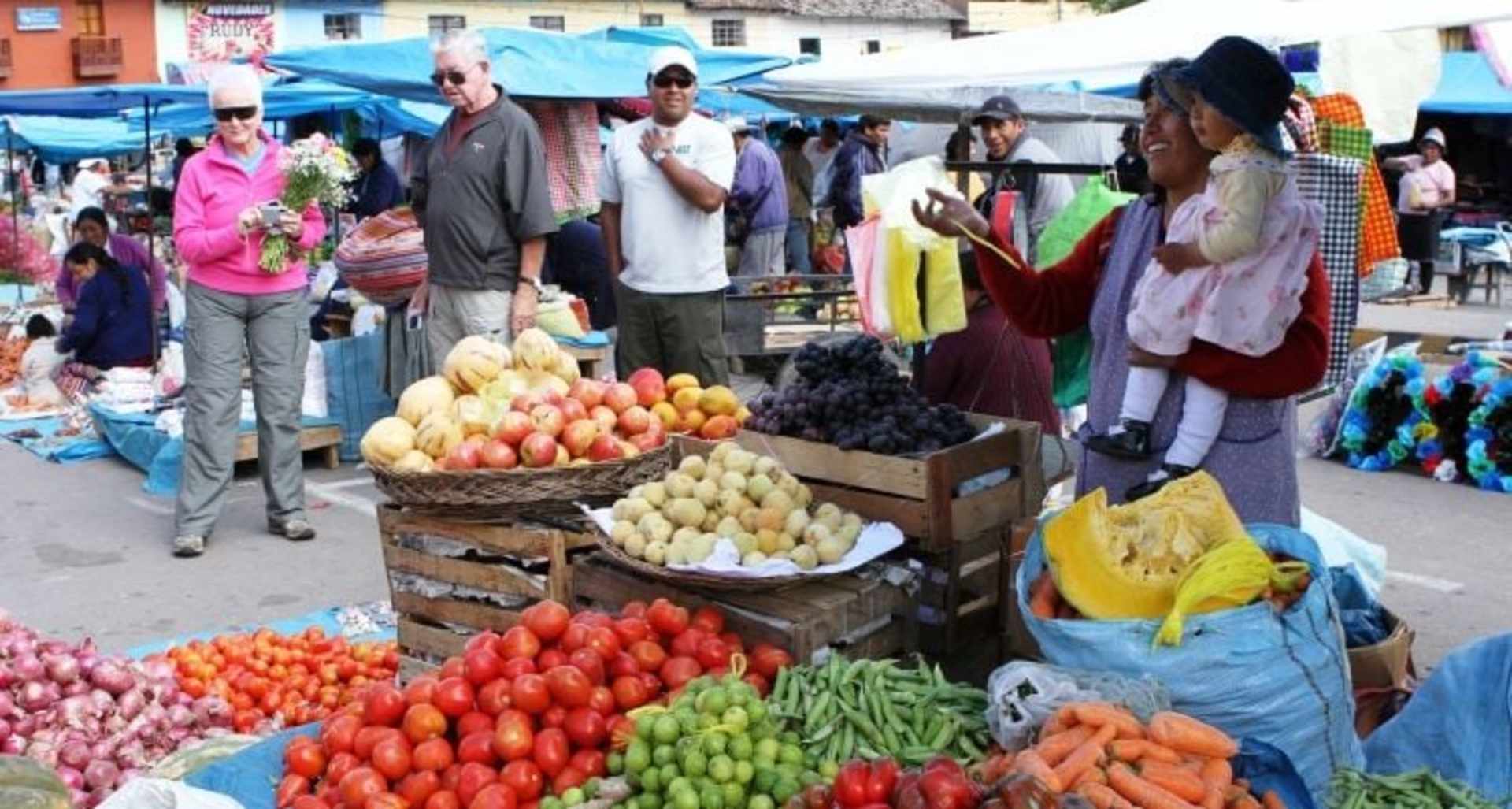 A bustling outdoor market with various stalls selling an array of colorful fruits and vegetables, surrounded by people browsing and shopping.