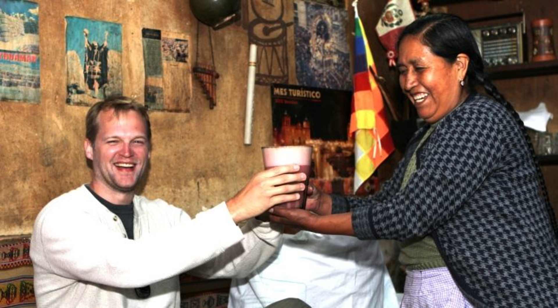 Two people, a man and a woman, are laughing and interacting in what appears to be a cozy, cluttered room filled with various decorations and memorabilia.