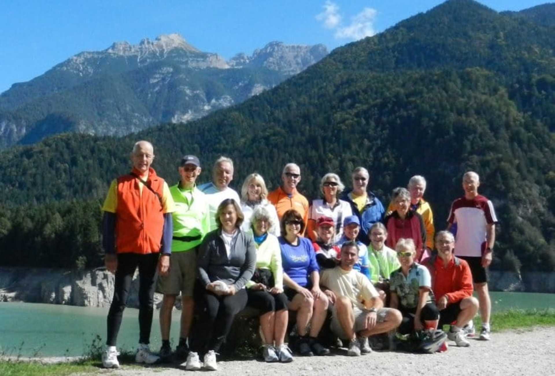 A group of people in colorful outdoor clothing standing together in front of a scenic mountain landscape.