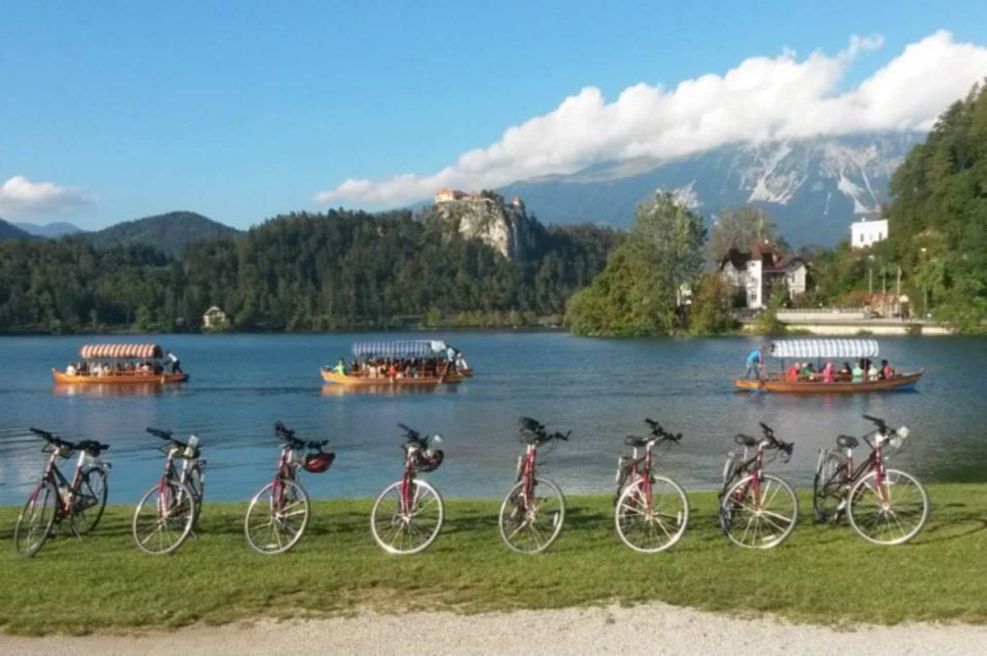 A scenic lakeside setting with colorful boats, bicycles lined up on the shore, and a picturesque mountain landscape in the background.
