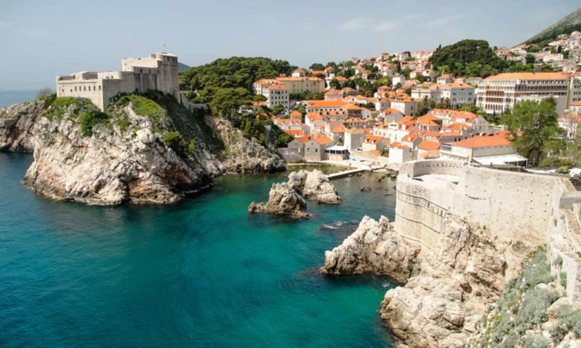 A picturesque coastal town nestled on steep cliffs, with vibrant orange-roofed buildings overlooking the turquoise waters of the sea below.