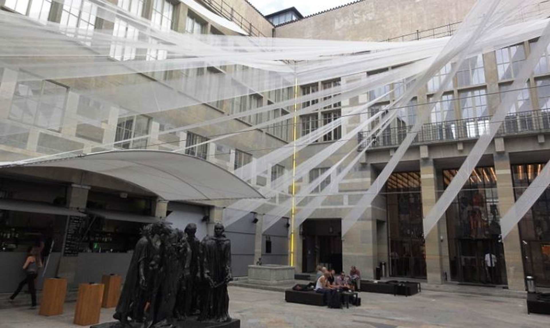 A large, open indoor space with a glass ceiling and walls, featuring various people and structures within it.