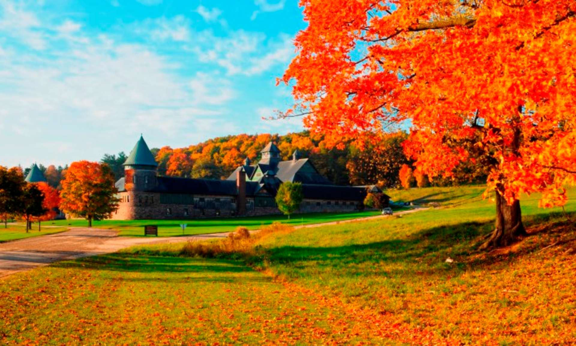 A picturesque autumn landscape with a grand castle-like building nestled among vibrant orange and red foliage, set against a backdrop of a clear blue sky.