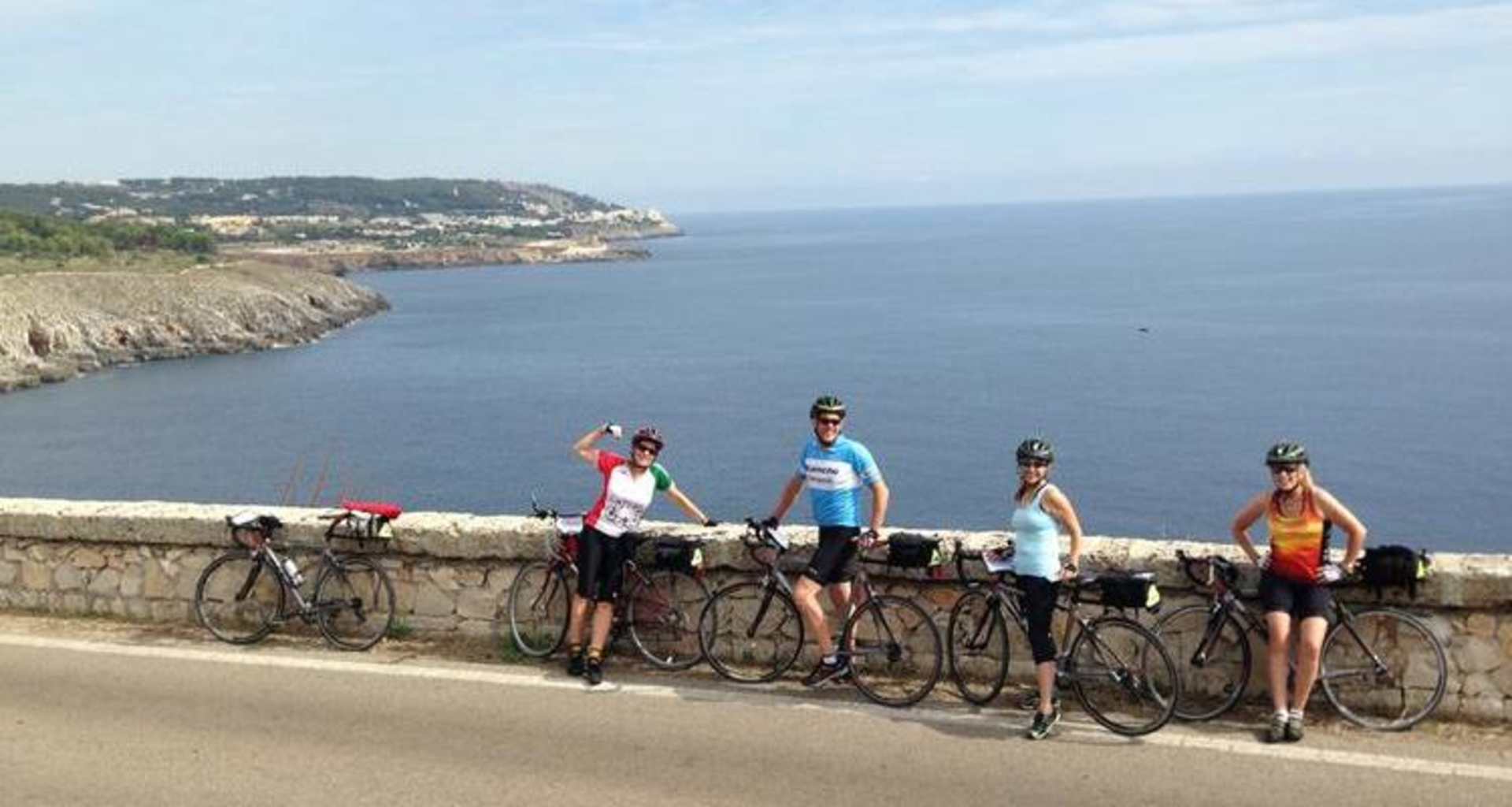 A group of cyclists riding their bicycles along a coastal road with a scenic ocean view in the background.