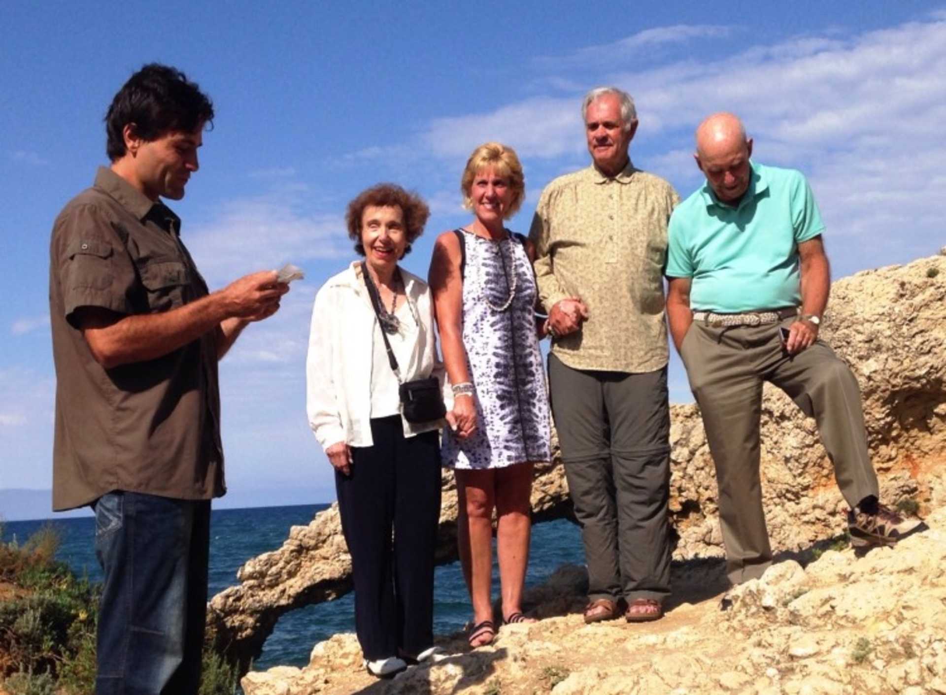 A group of five people, three women and two men, standing together on a rocky coastal area with the ocean visible in the background.