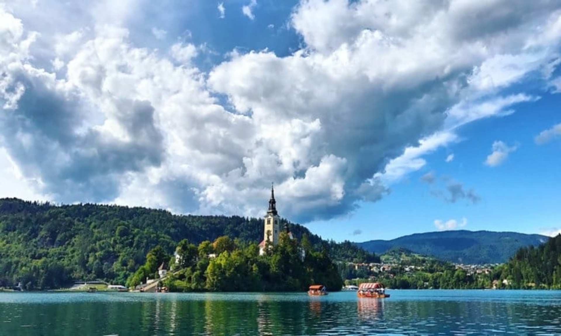 A picturesque lake surrounded by lush green forests and mountains, with a majestic castle-like structure standing tall on the shore, reflected in the calm waters.